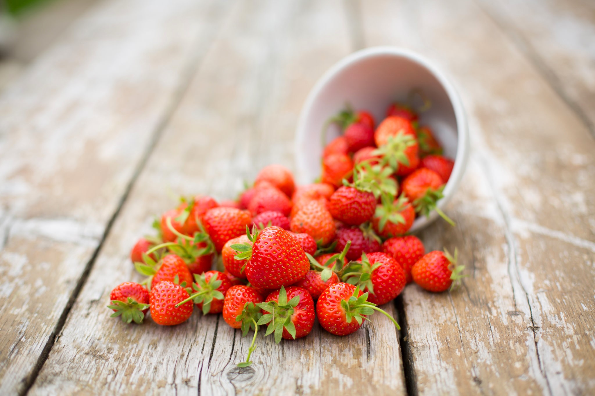 Strawberries spilled from a bowl onto a wooden table HD Wallpaper