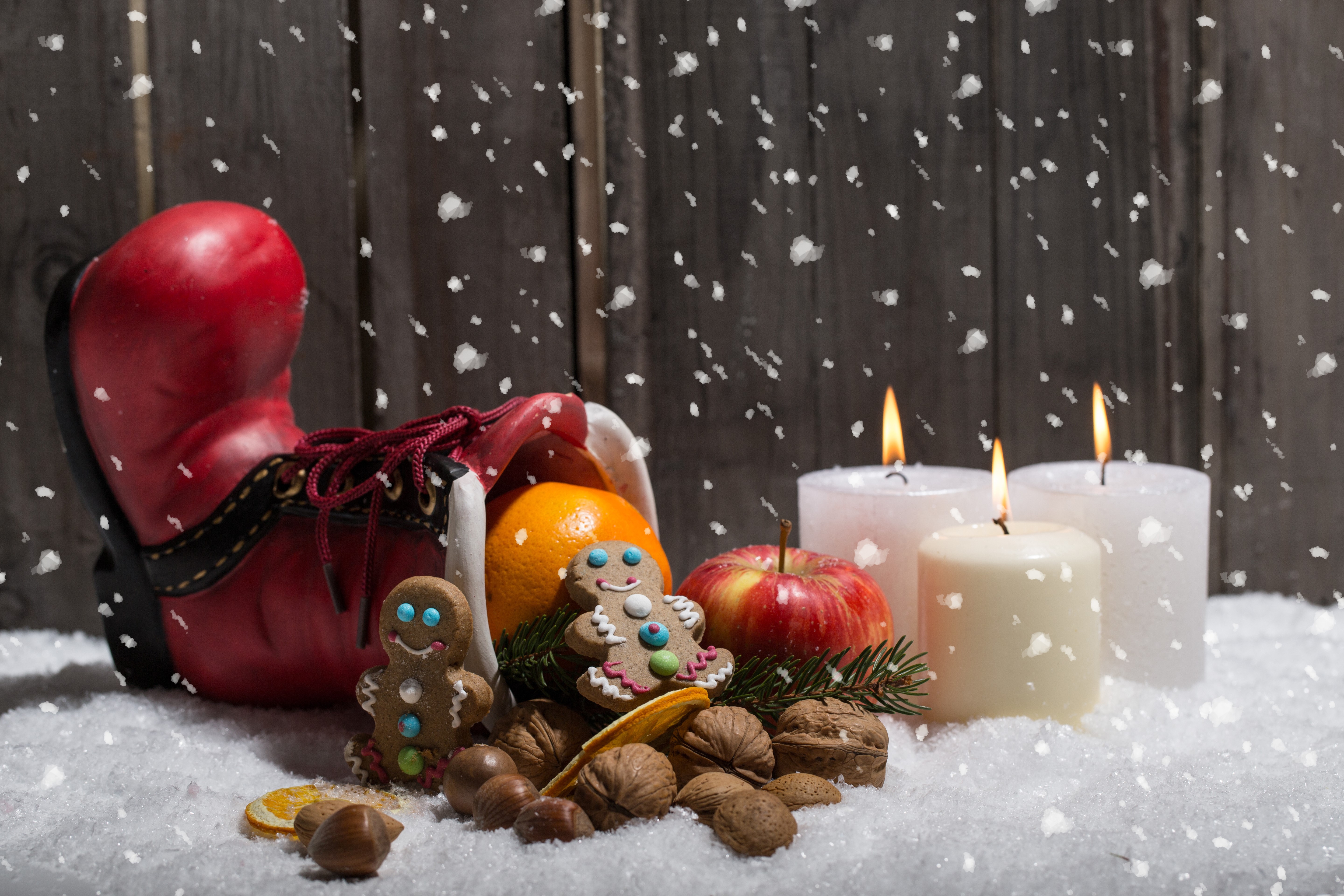 Christmas boot with fruit, cookies, candles, and nuts in snow HD Wallpaper