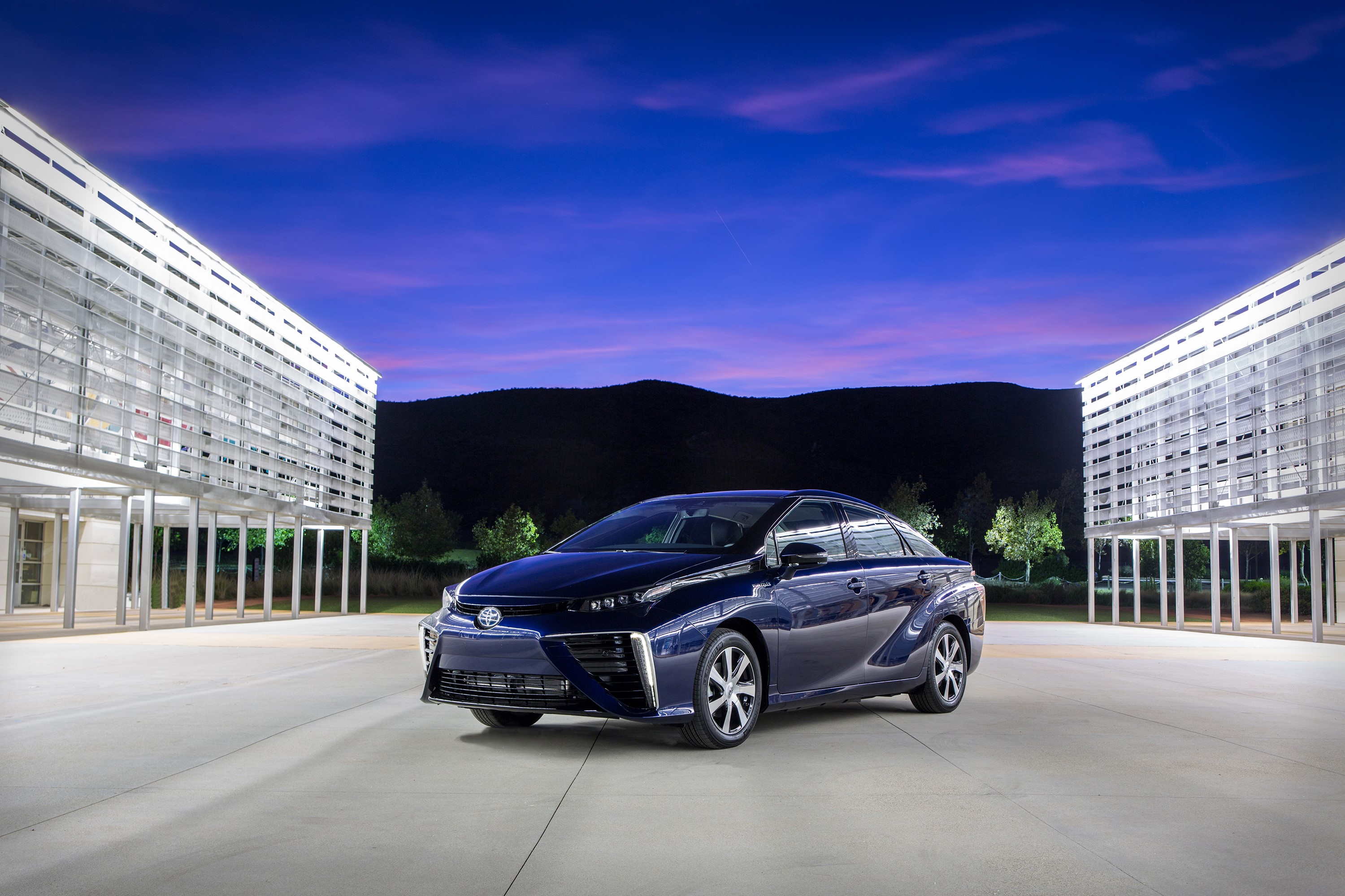 Blue 2015 Toyota Mirai parked outside modern buildings at dusk HD Wallpaper