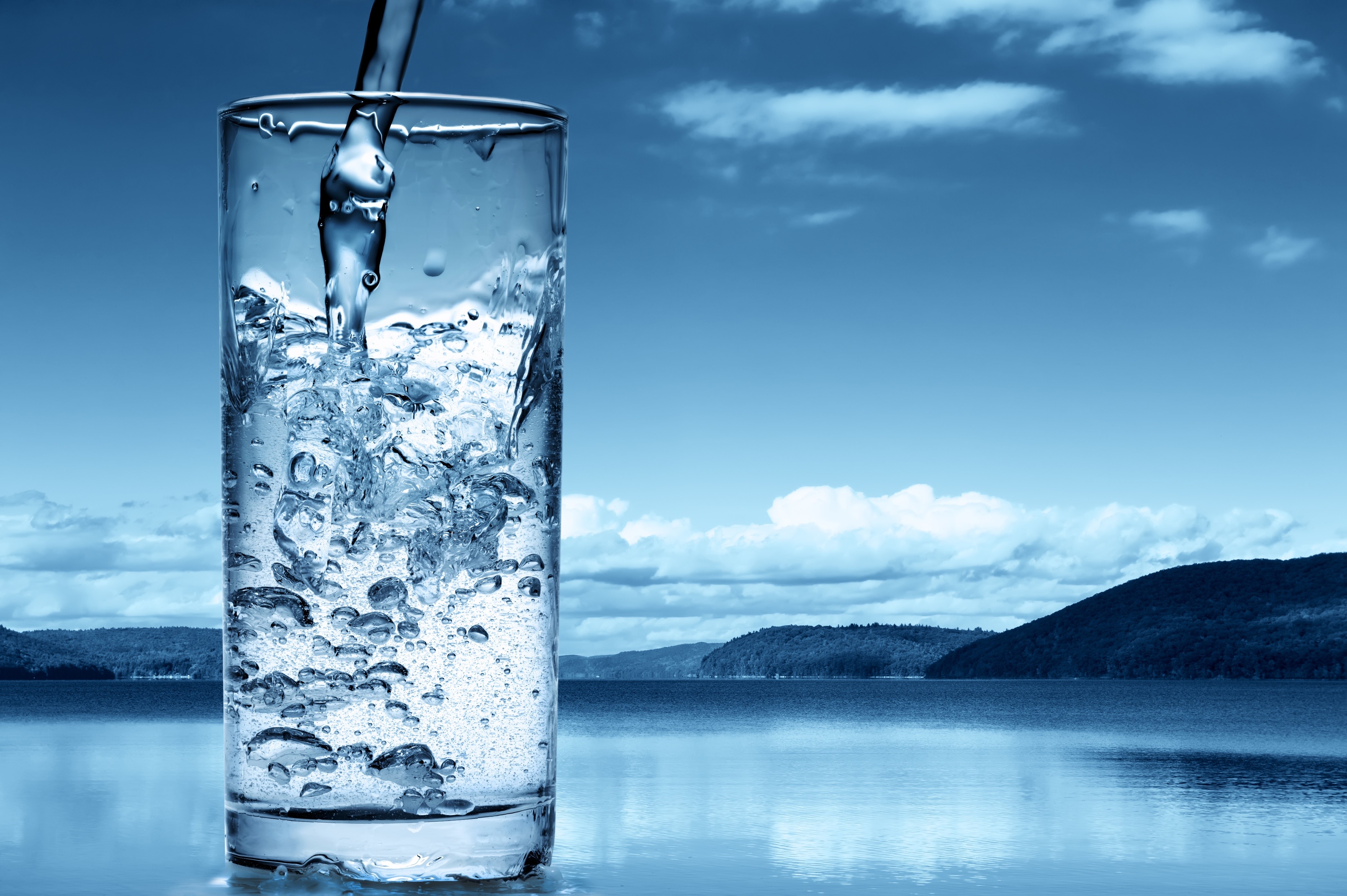 Water being poured into a glass with a lake and sky background HD Wallpaper