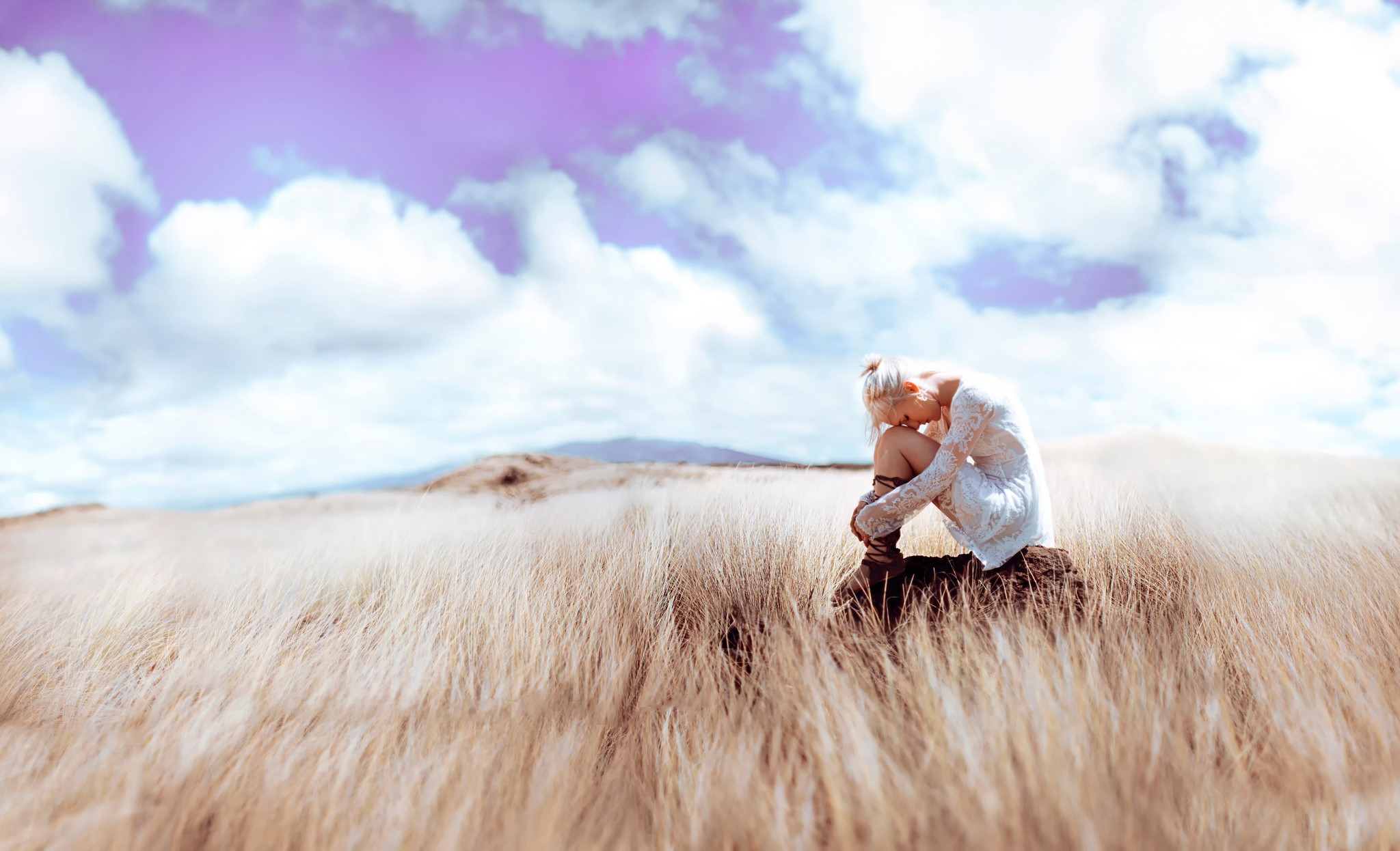 Blonde girl sitting in tall grass under purple sky HD Wallpaper