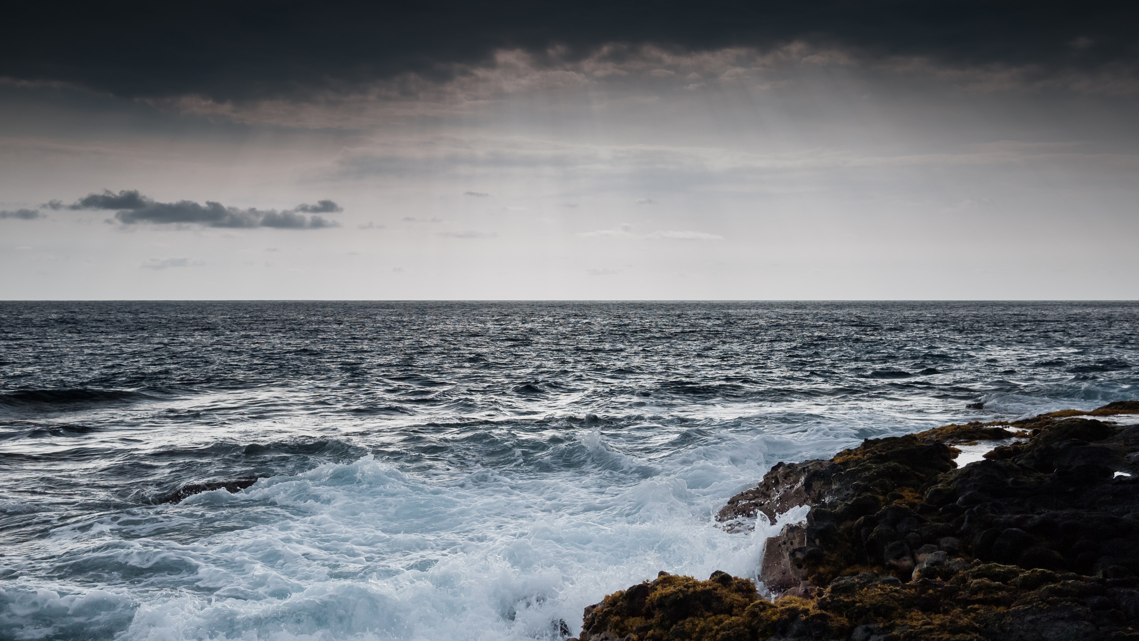 Waves crashing on rocky shore under cloudy sky HD Wallpaper