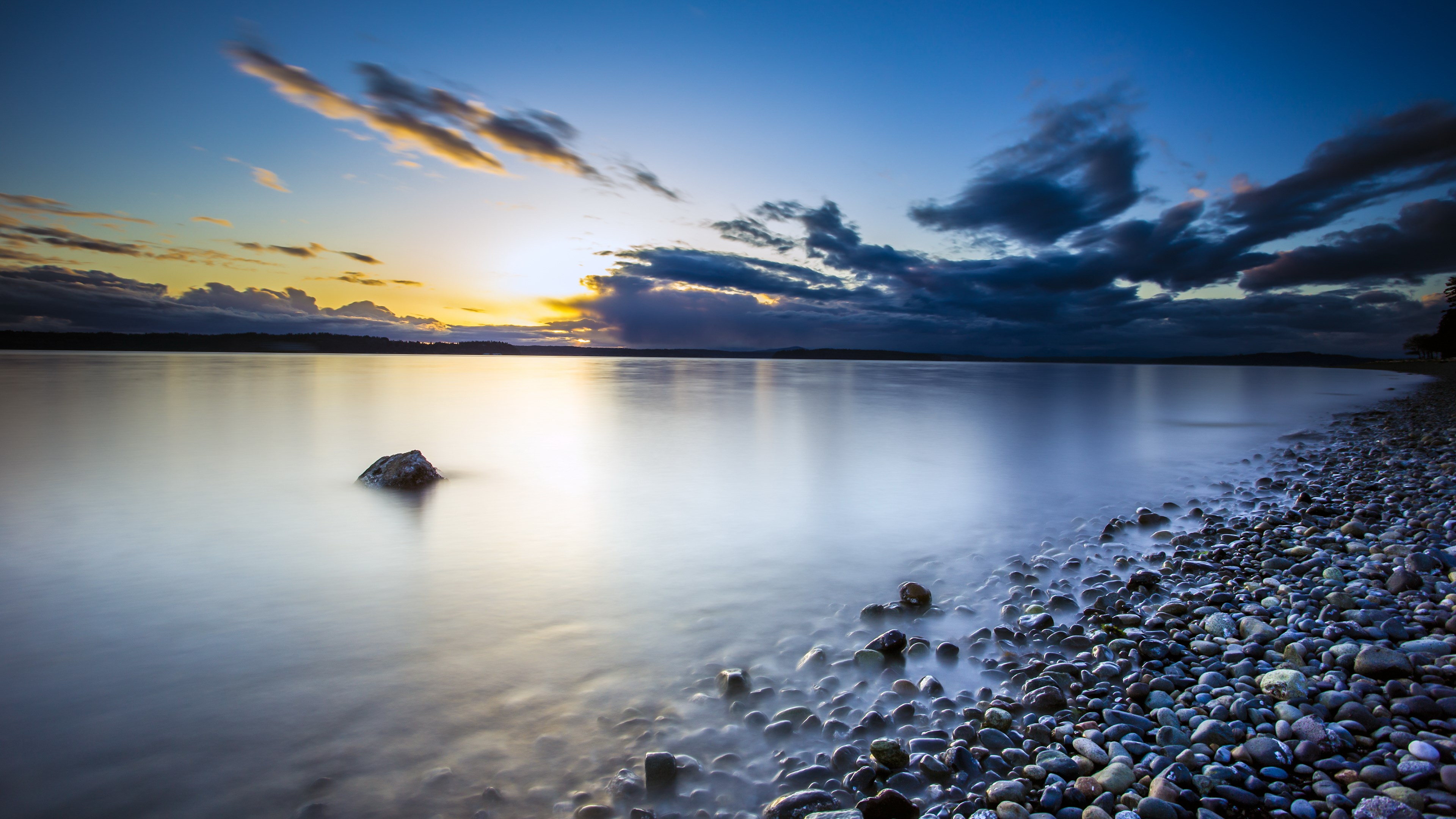 Sunset over a rocky shore with calm water HD Wallpaper