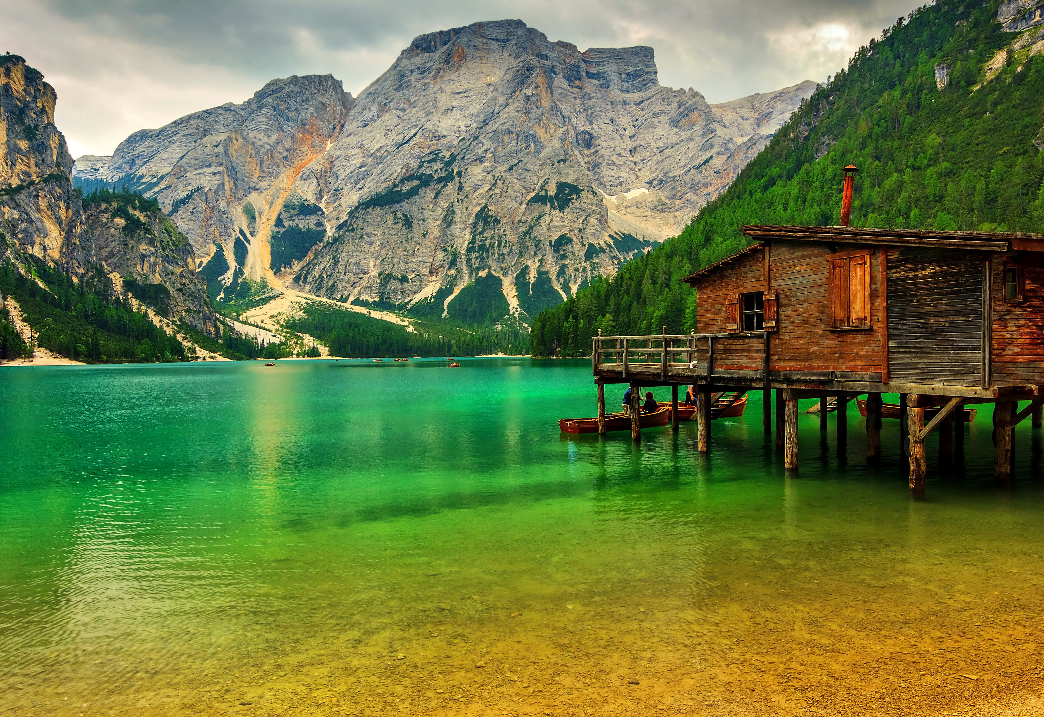 Wooden cabin on stilts by a turquoise lake with mountains HD Wallpaper