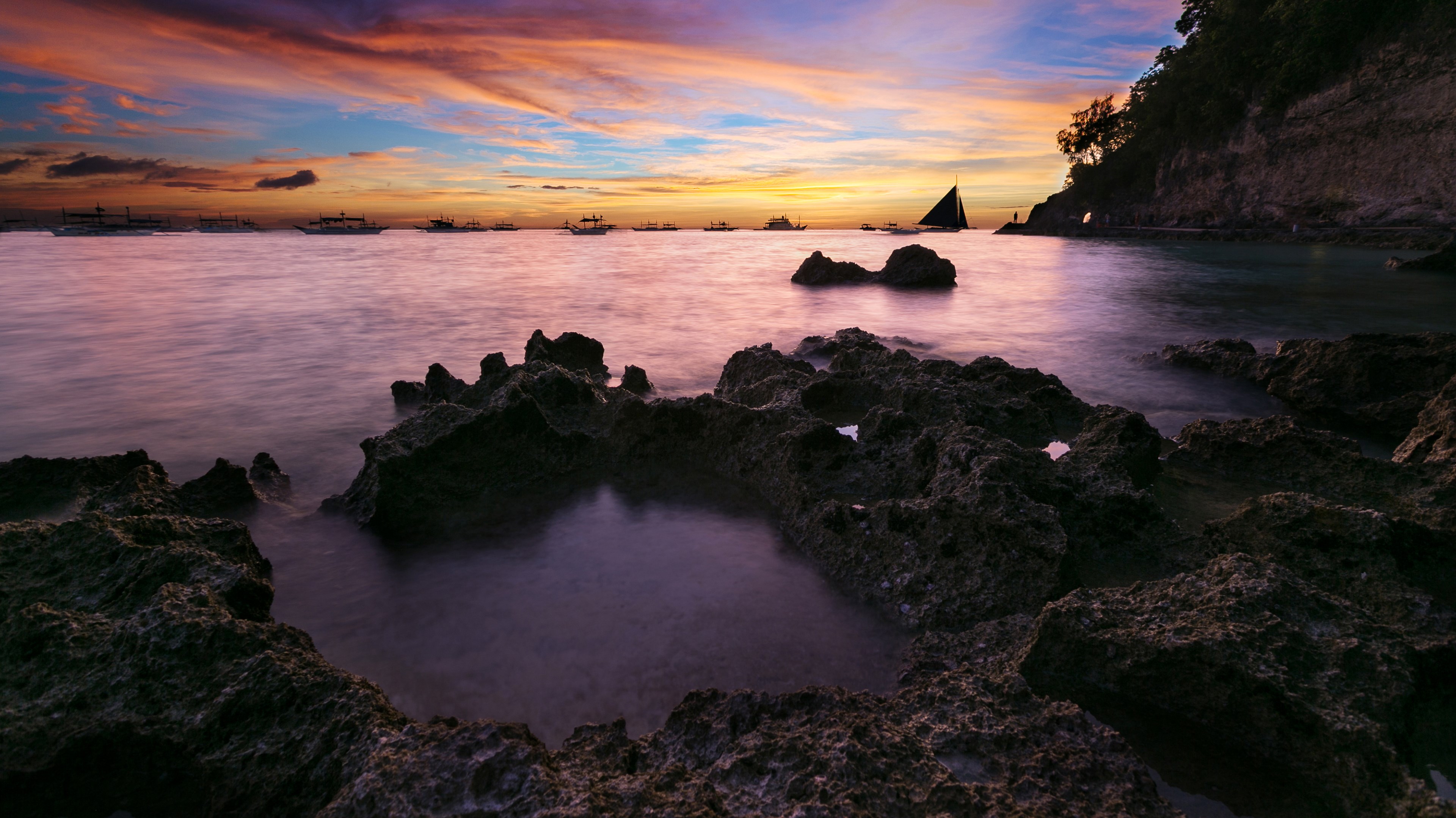 Sunset over rocky shore with boats and sailboat HD Wallpaper
