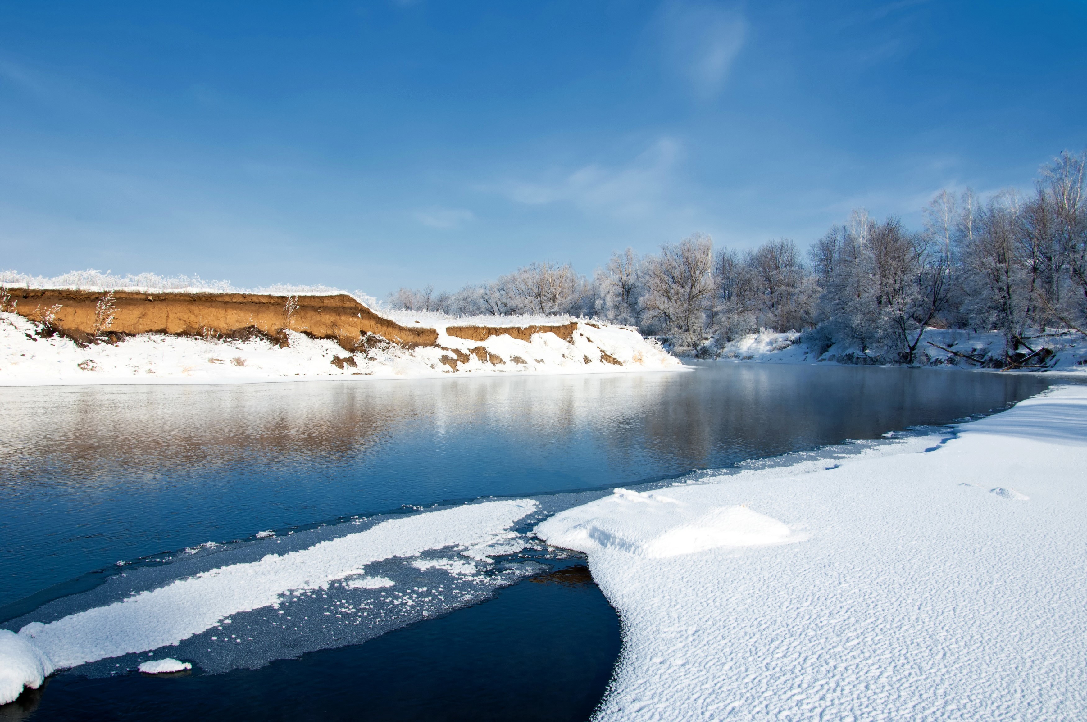 Winter riverbank with snow and ice under a blue sky HD Wallpaper