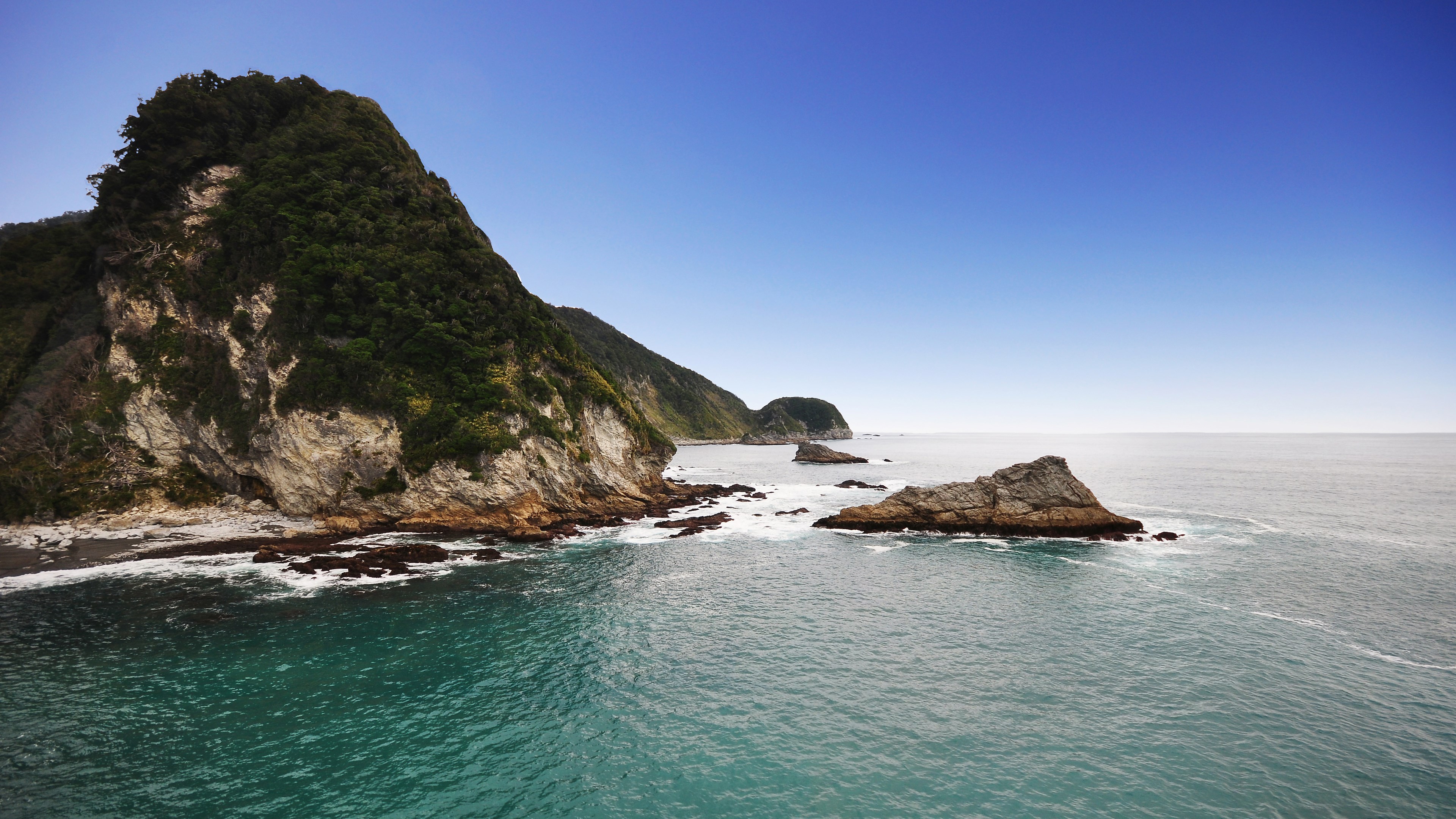 Rocky coastline with green mountains and blue sky HD Wallpaper