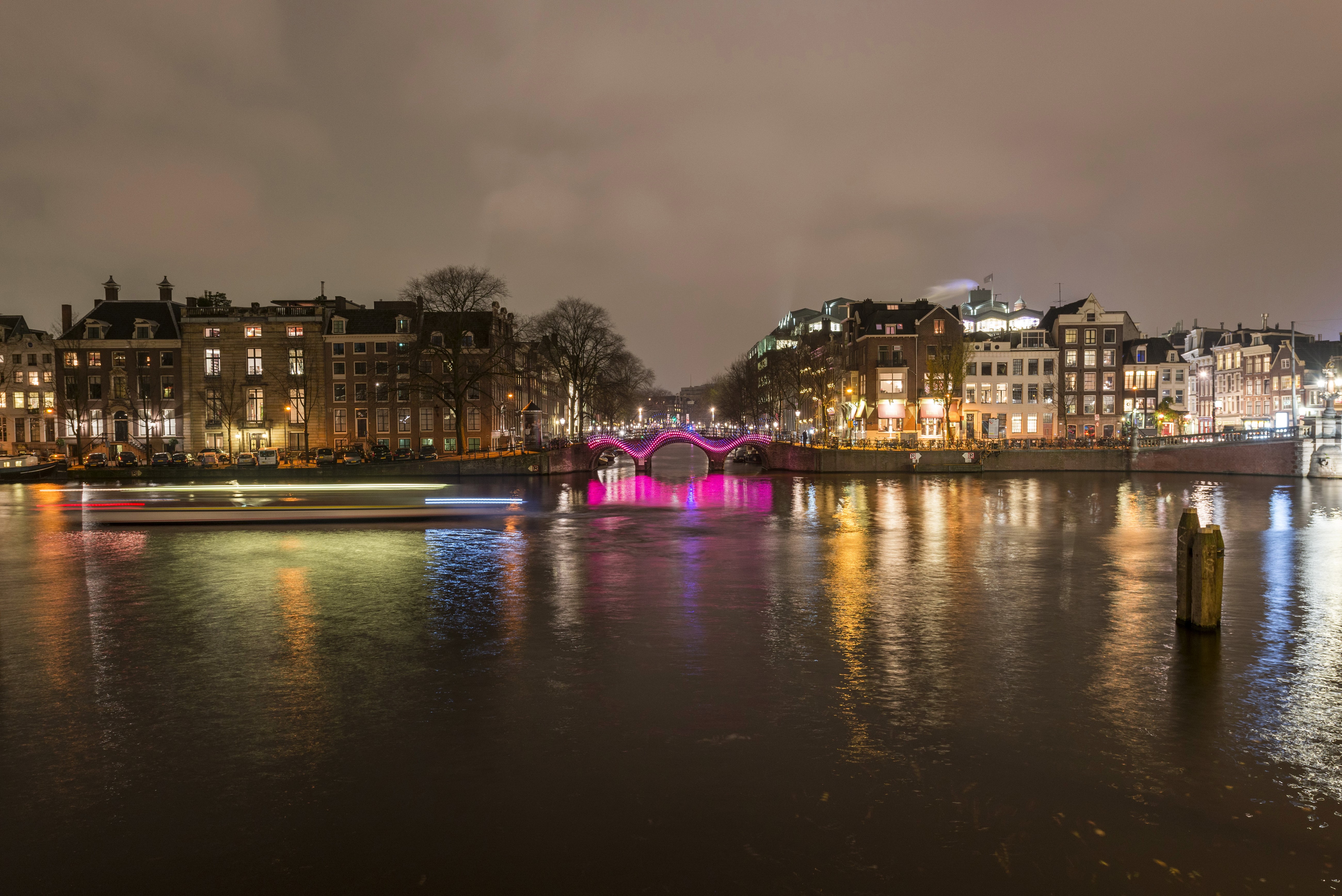 Amsterdam canal at night with illuminated bridge and boat HD Wallpaper