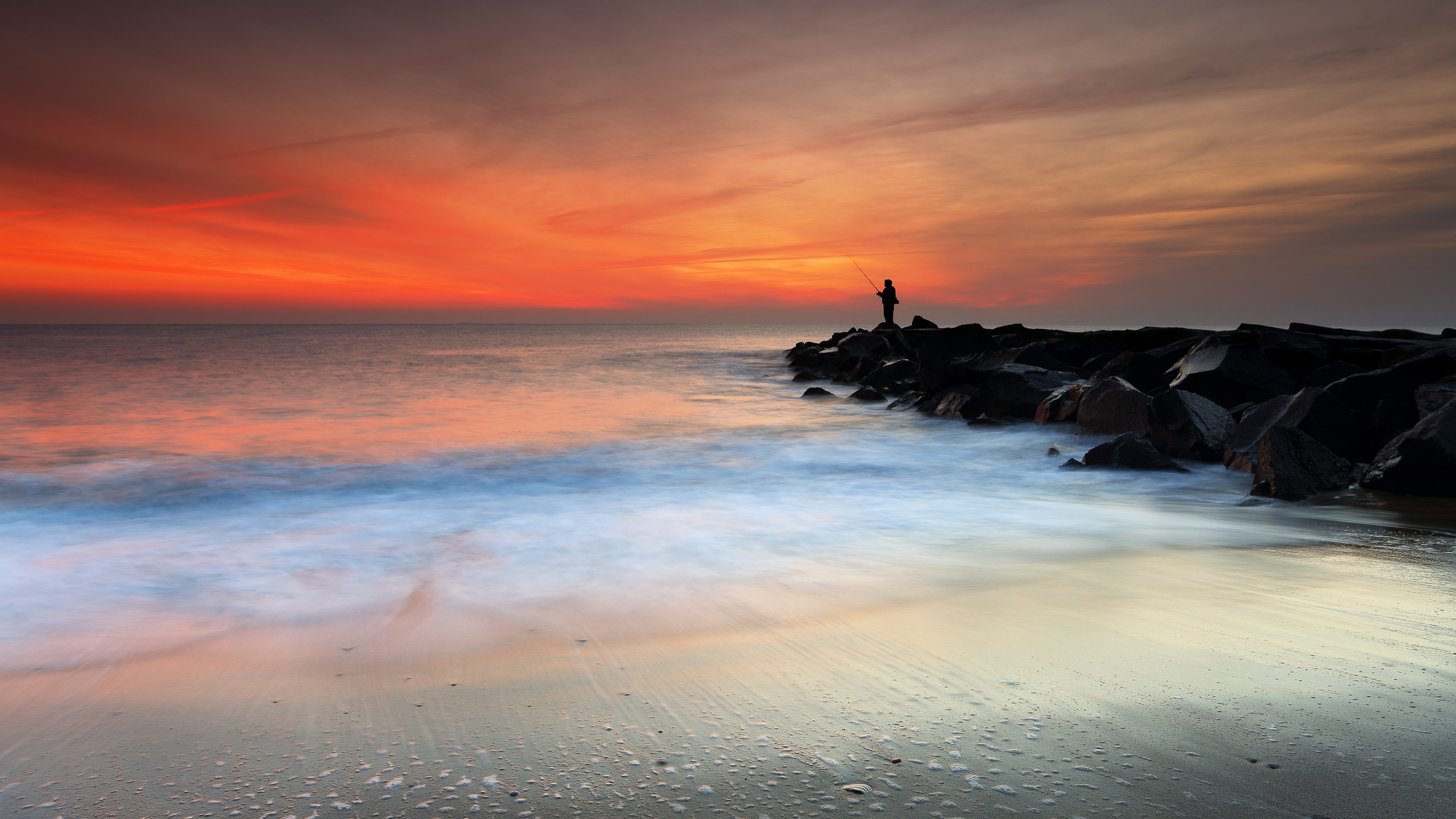 Fisherman on rocks at sunset with ocean waves HD Wallpaper