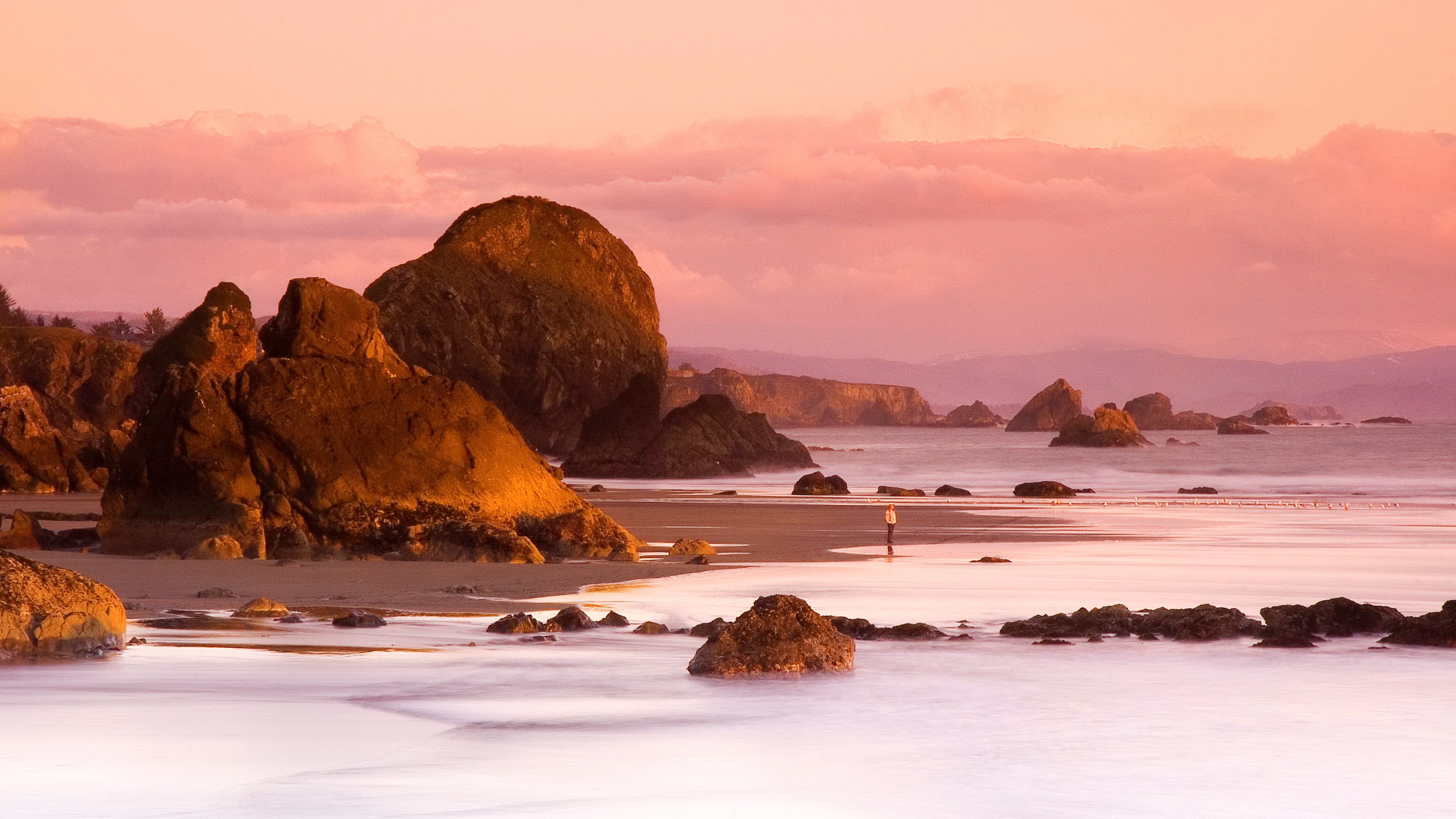 Sunset over a rocky beach with a lone figure HD Wallpaper