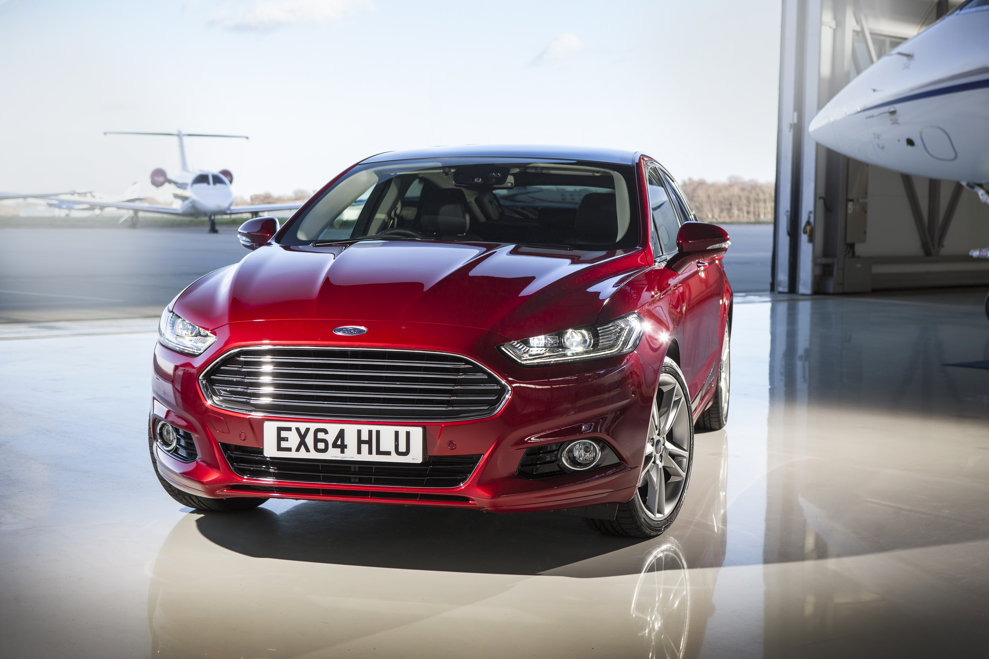 Red Ford Mondeo parked in hangar with private jets HD Wallpaper