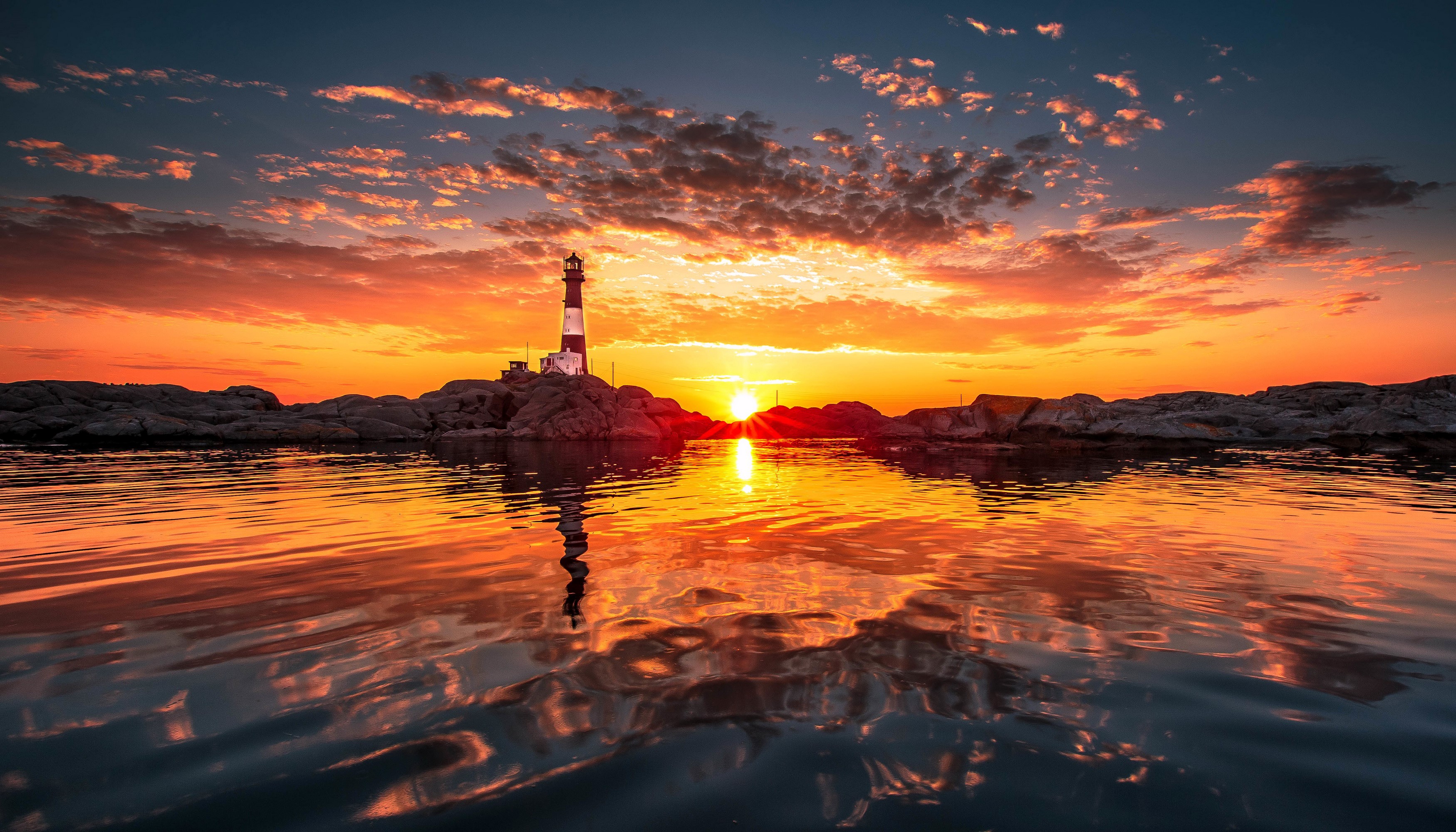 Lighthouse on rocky shore during sunset with reflection HD Wallpaper