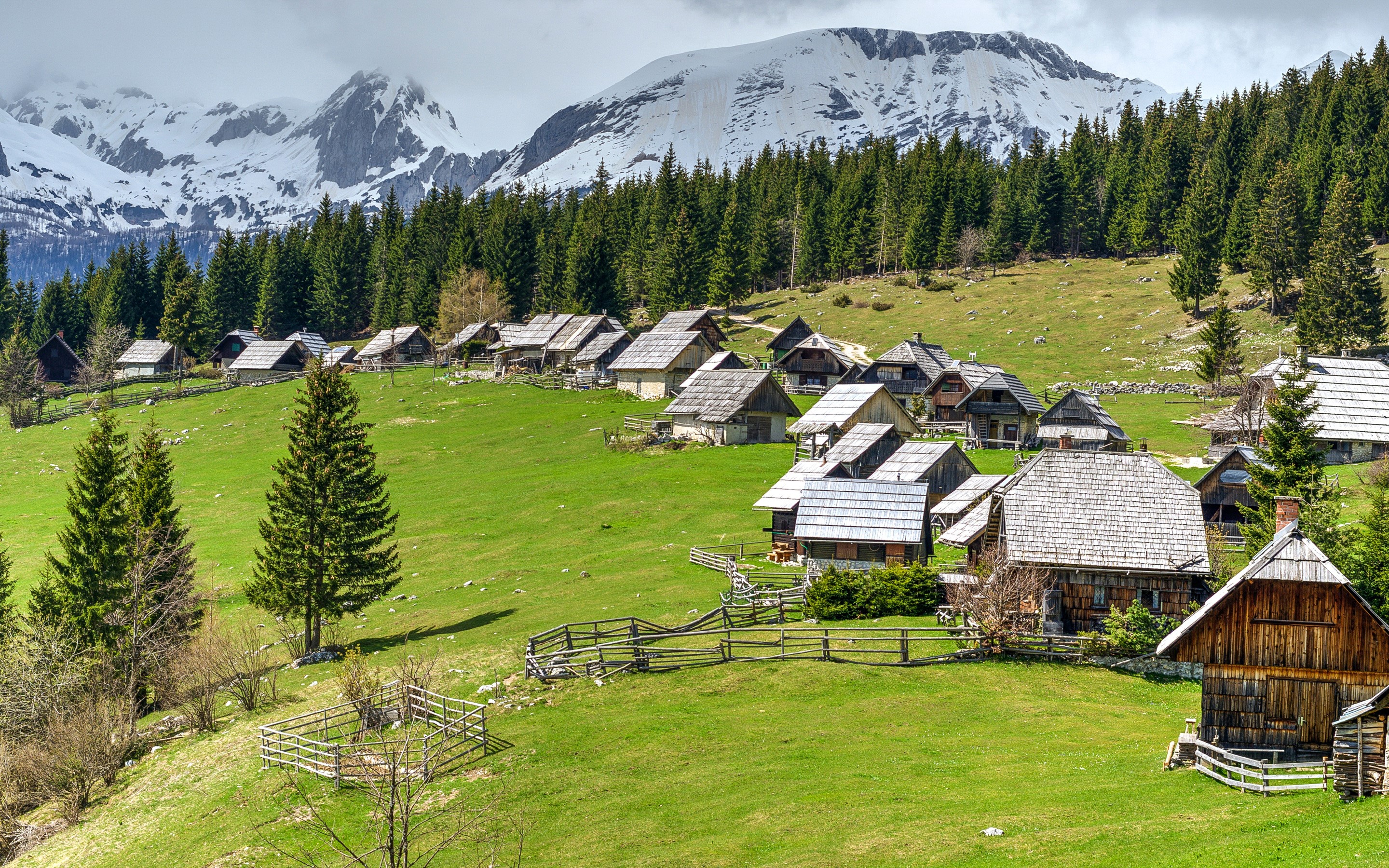 Mountain village with wooden houses and snowy peaks in Slovenia HD Wallpaper
