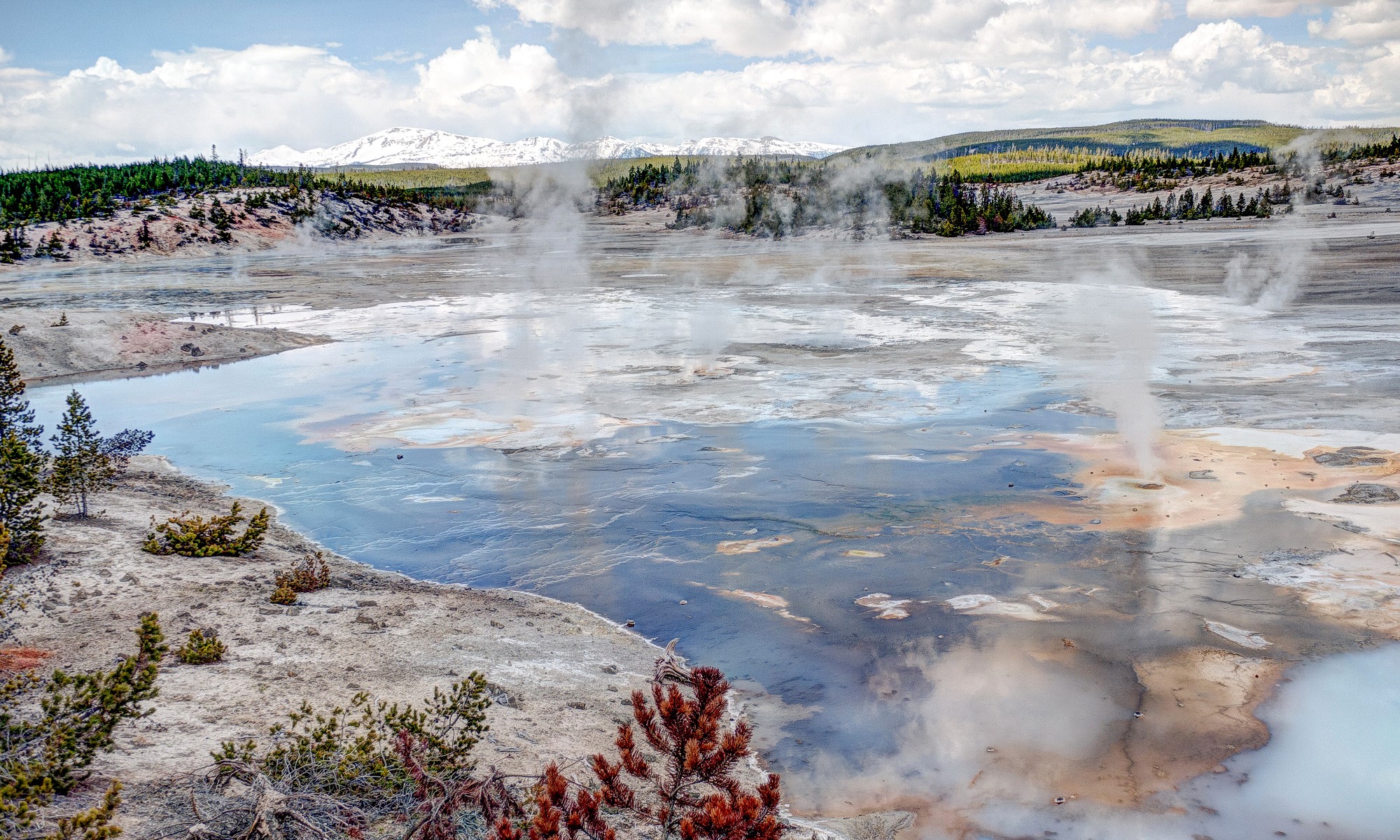 Geothermal landscape with steaming pools and snow-capped mountains HD Wallpaper