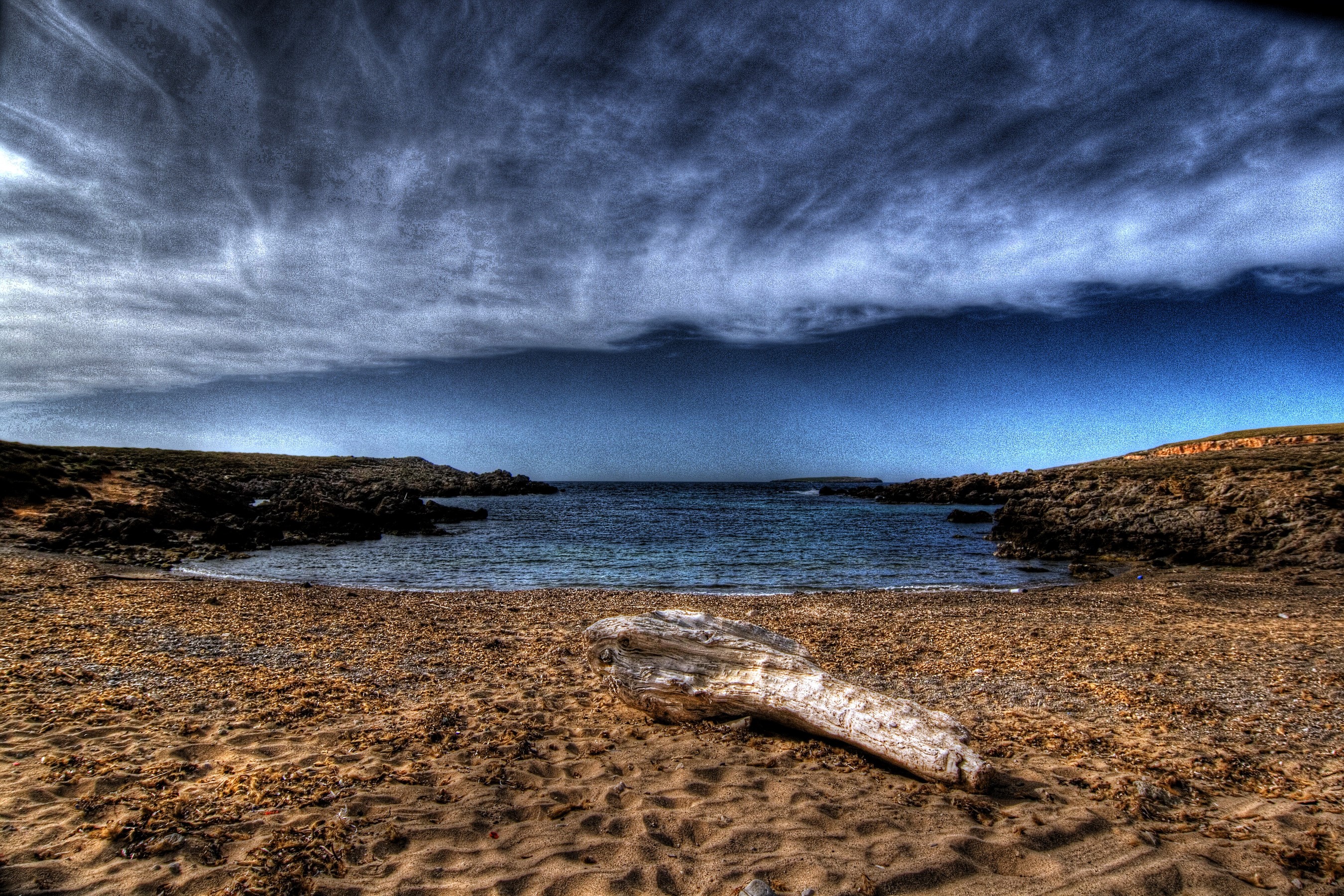 Beach with driftwood and dramatic sky in Balearic Islands, Spain HD Wallpaper
