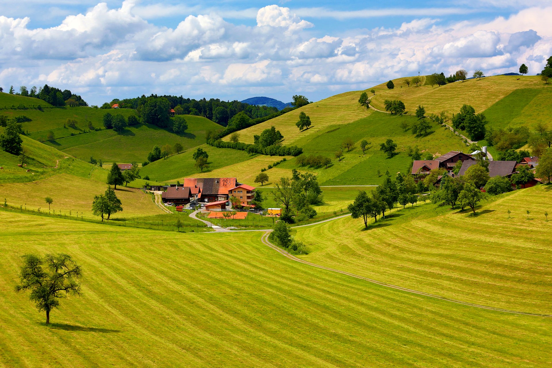 Green rolling hills with a village and clouds HD Wallpaper