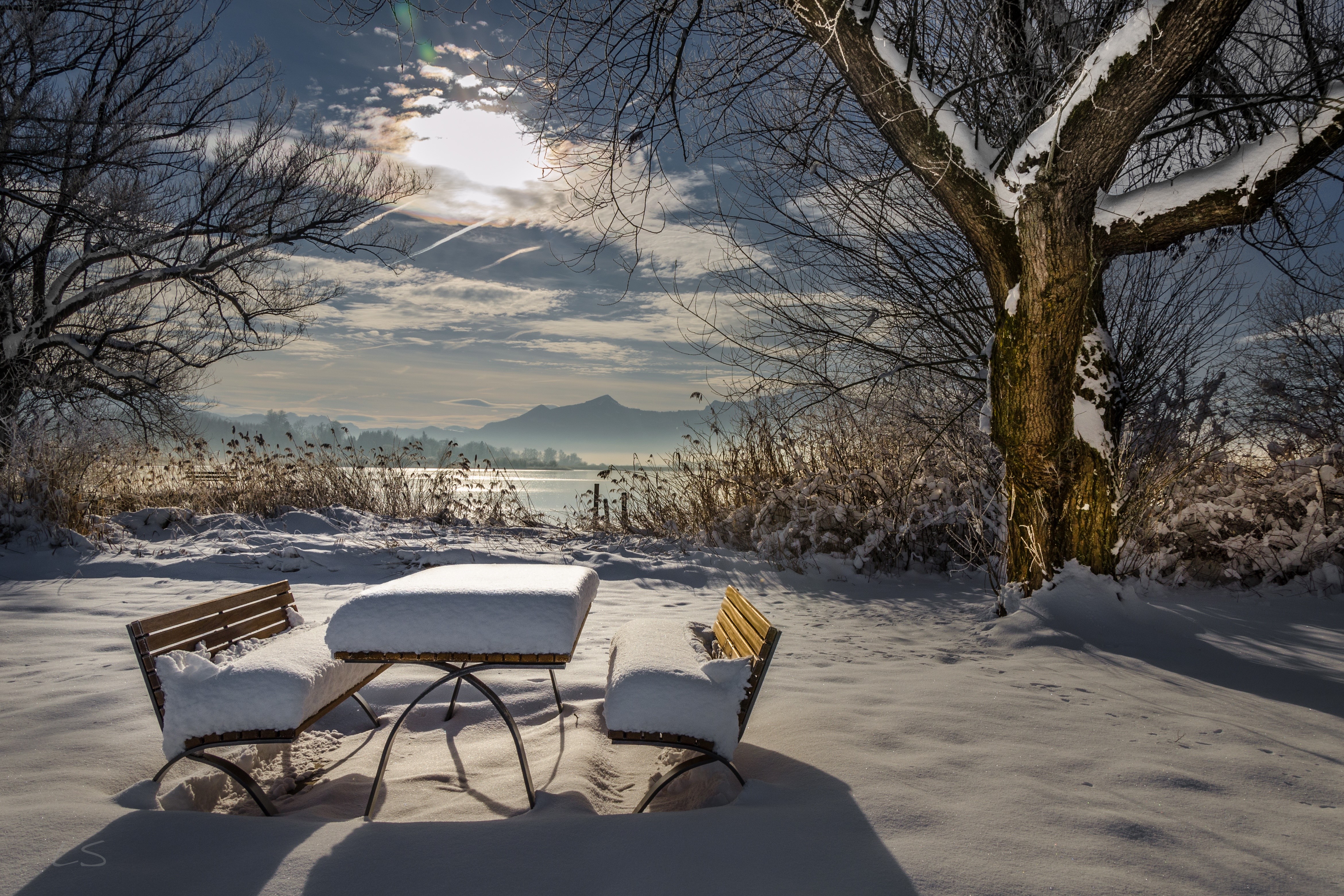 Winter scene with snow-covered table and benches by a lake HD Wallpaper