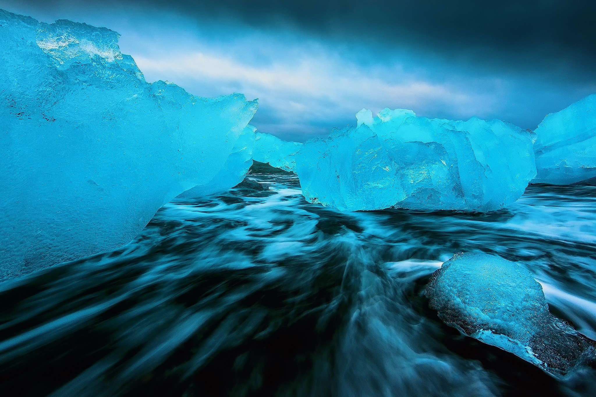 Blue icebergs on a black sand beach with ocean waves HD Wallpaper