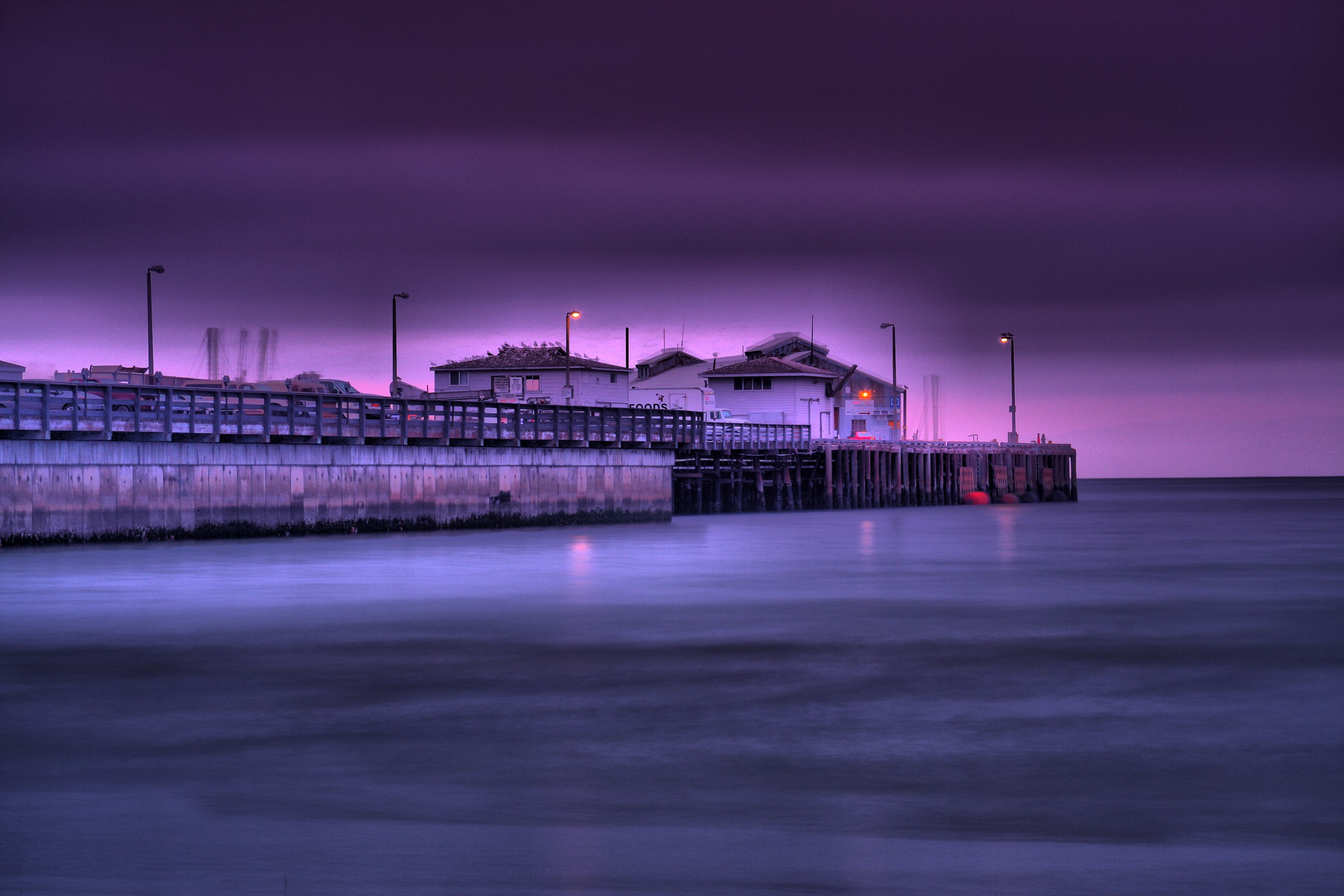 Pier with buildings and street lights over the sea at dusk HD Wallpaper