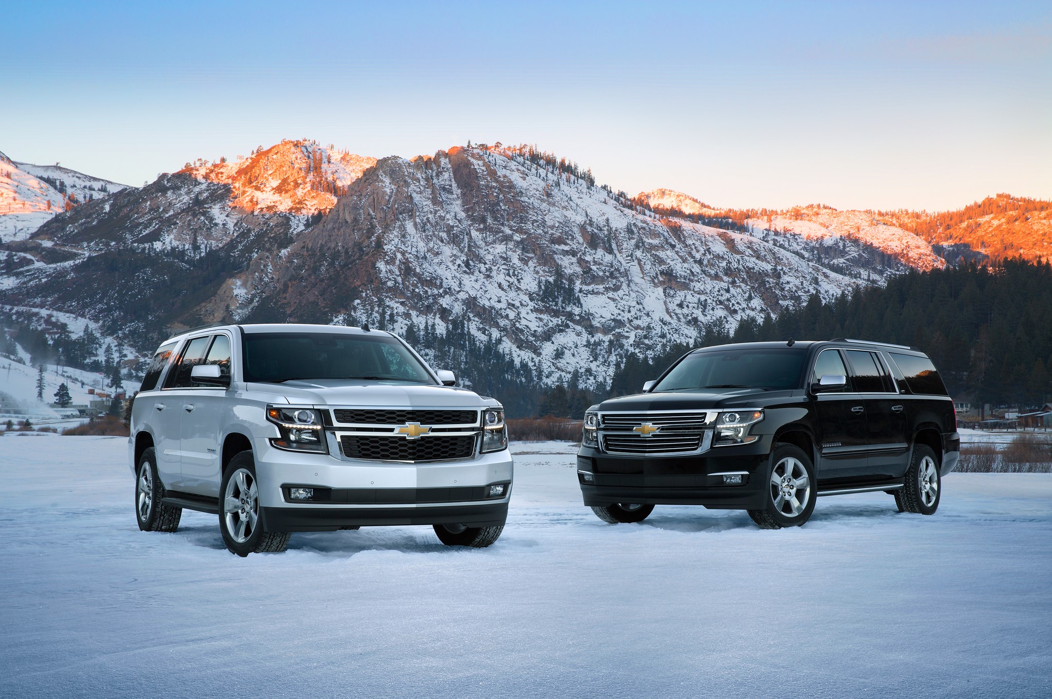 Two Chevrolet Suburbans in a Snowy Mountain Landscape HD Wallpaper