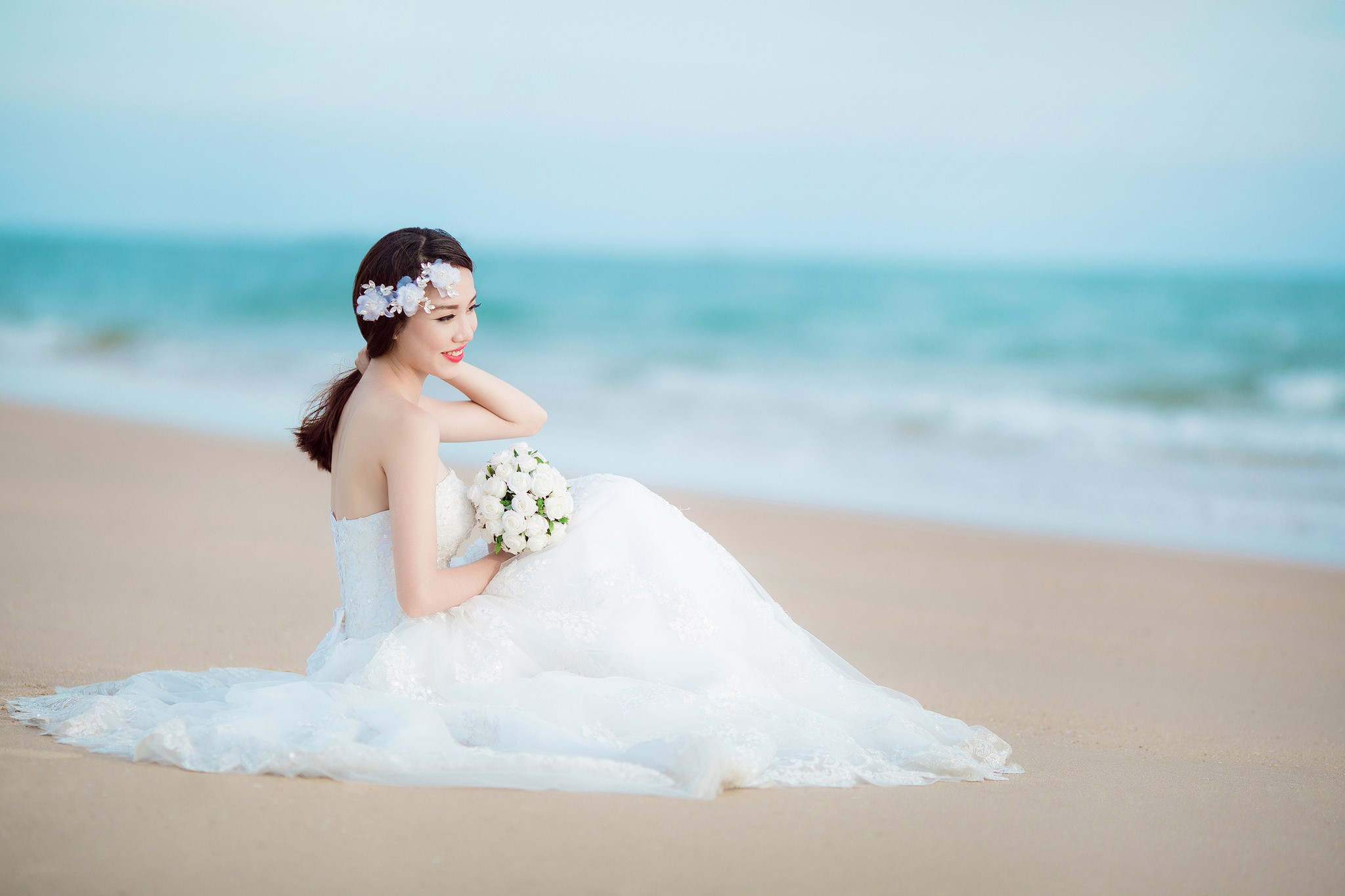 Bride in Wedding Dress Sitting on Beach with Bouquet HD Wallpaper