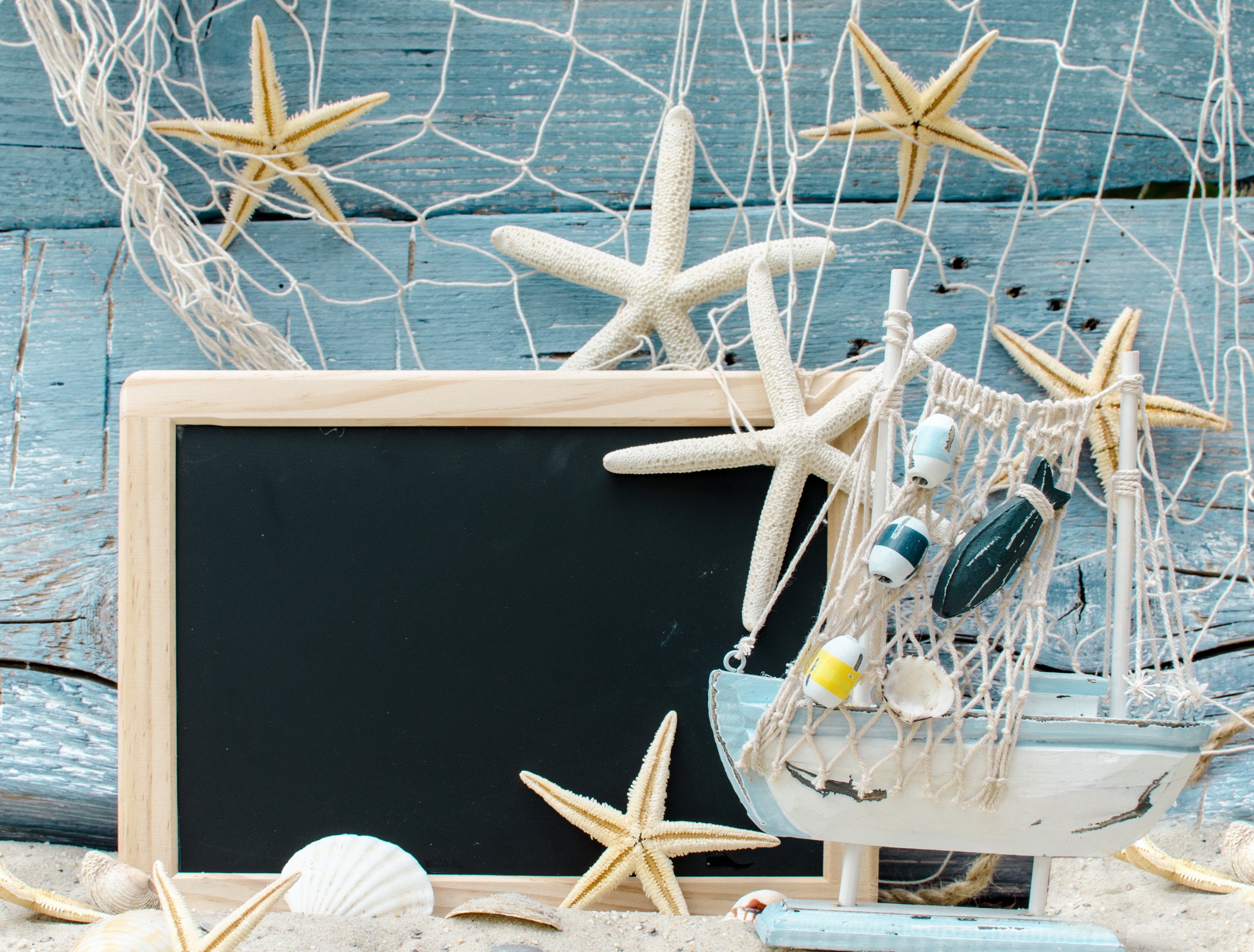 Beach scene with starfish, seashells, and a model boat HD Wallpaper