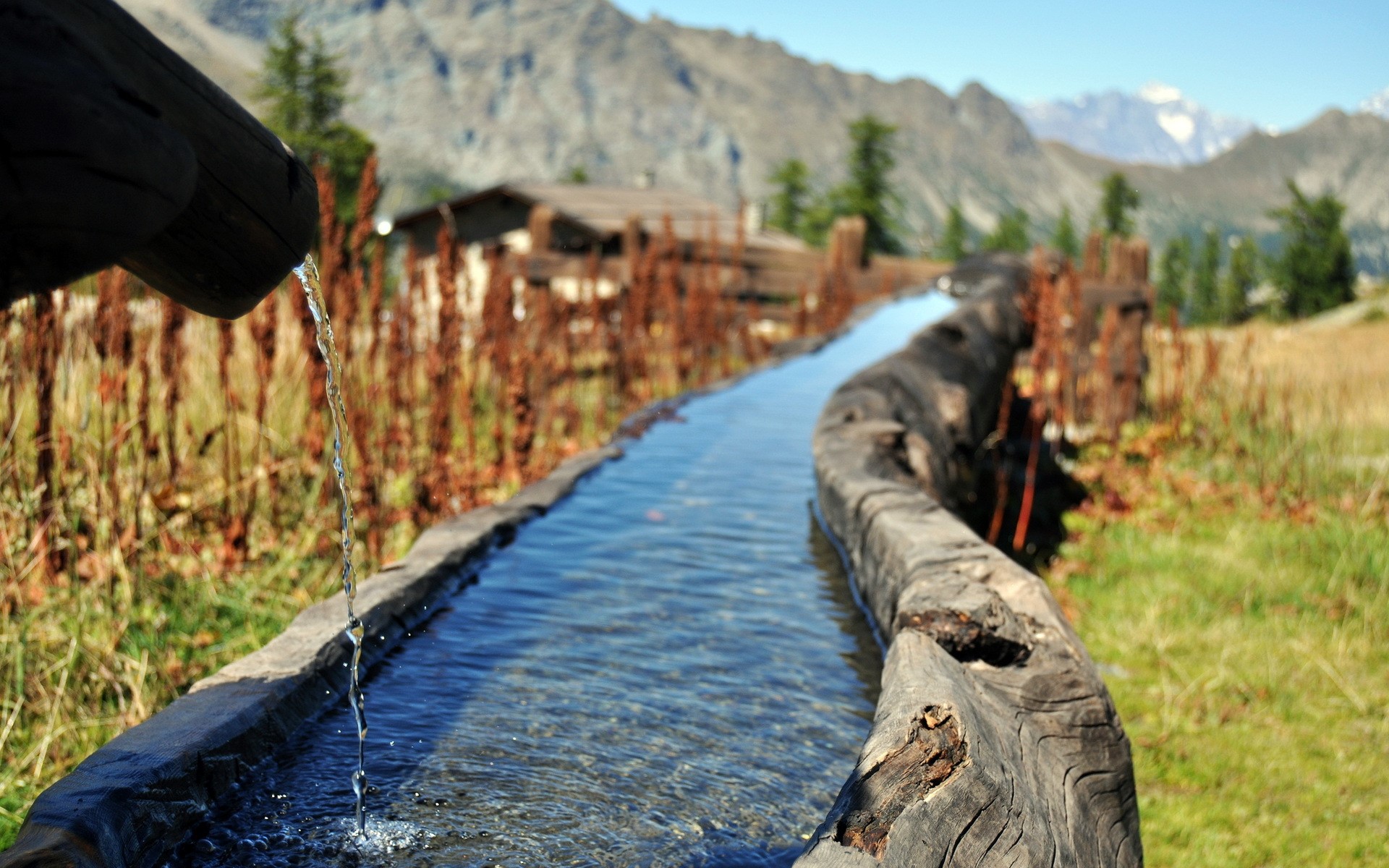 Water flowing through a wooden trough in the mountains HD Wallpaper