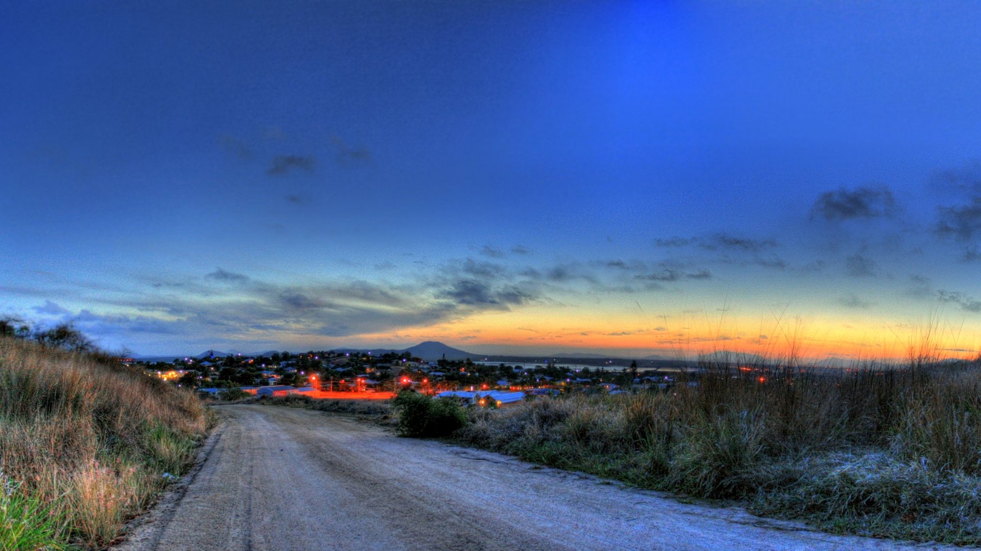 Dirt road leading to a town at sunset HD Wallpaper