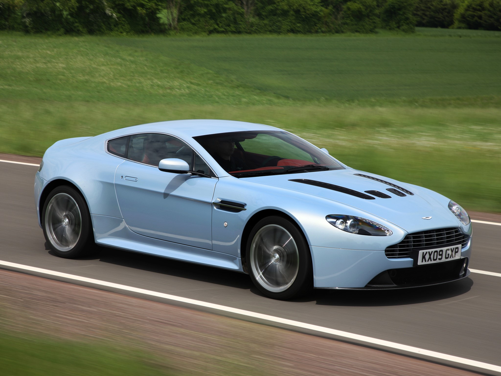 Aston Martin V12 driving on a road HD Wallpaper