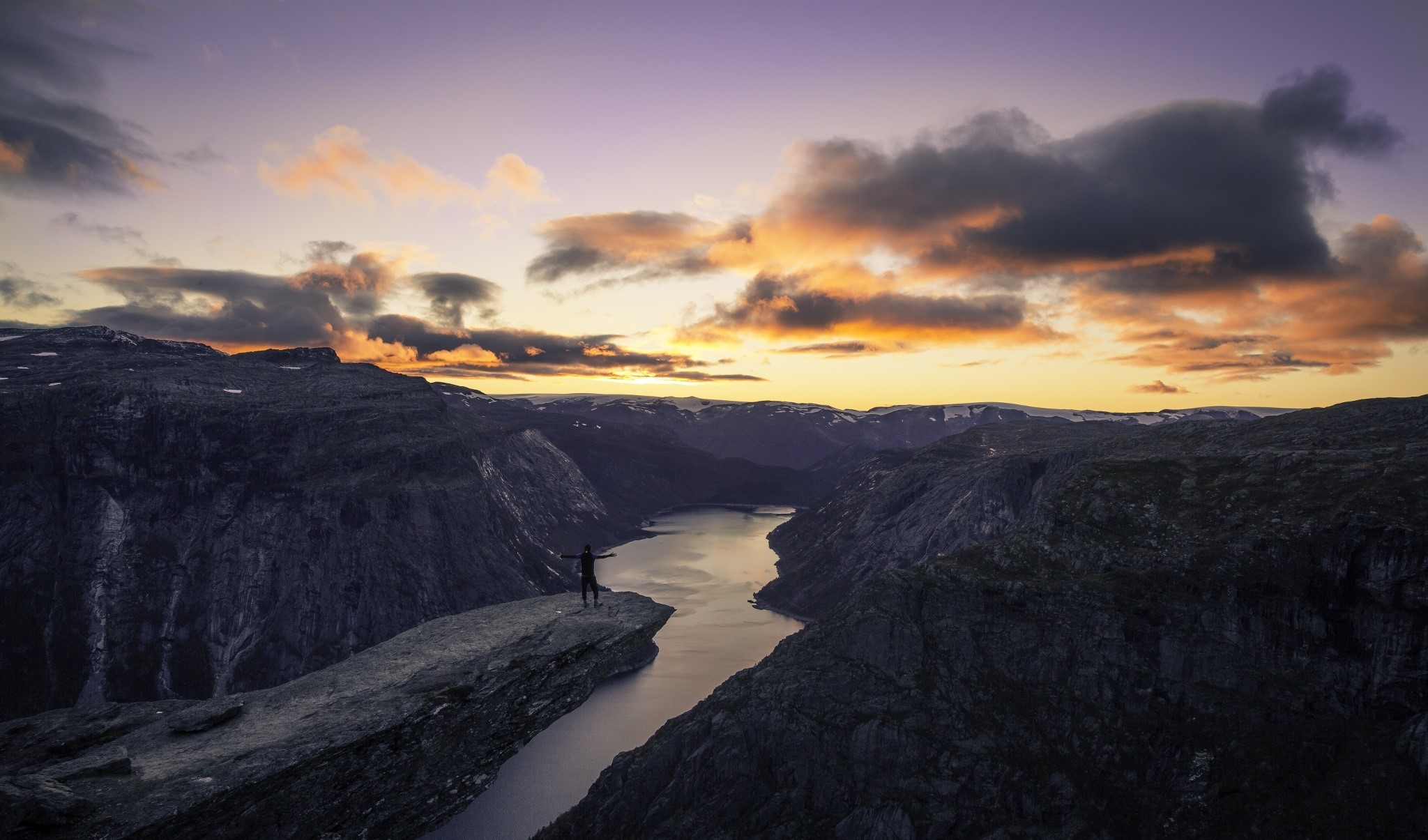 Person standing on Trolltunga cliff overlooking a fjord at sunset HD Wallpaper