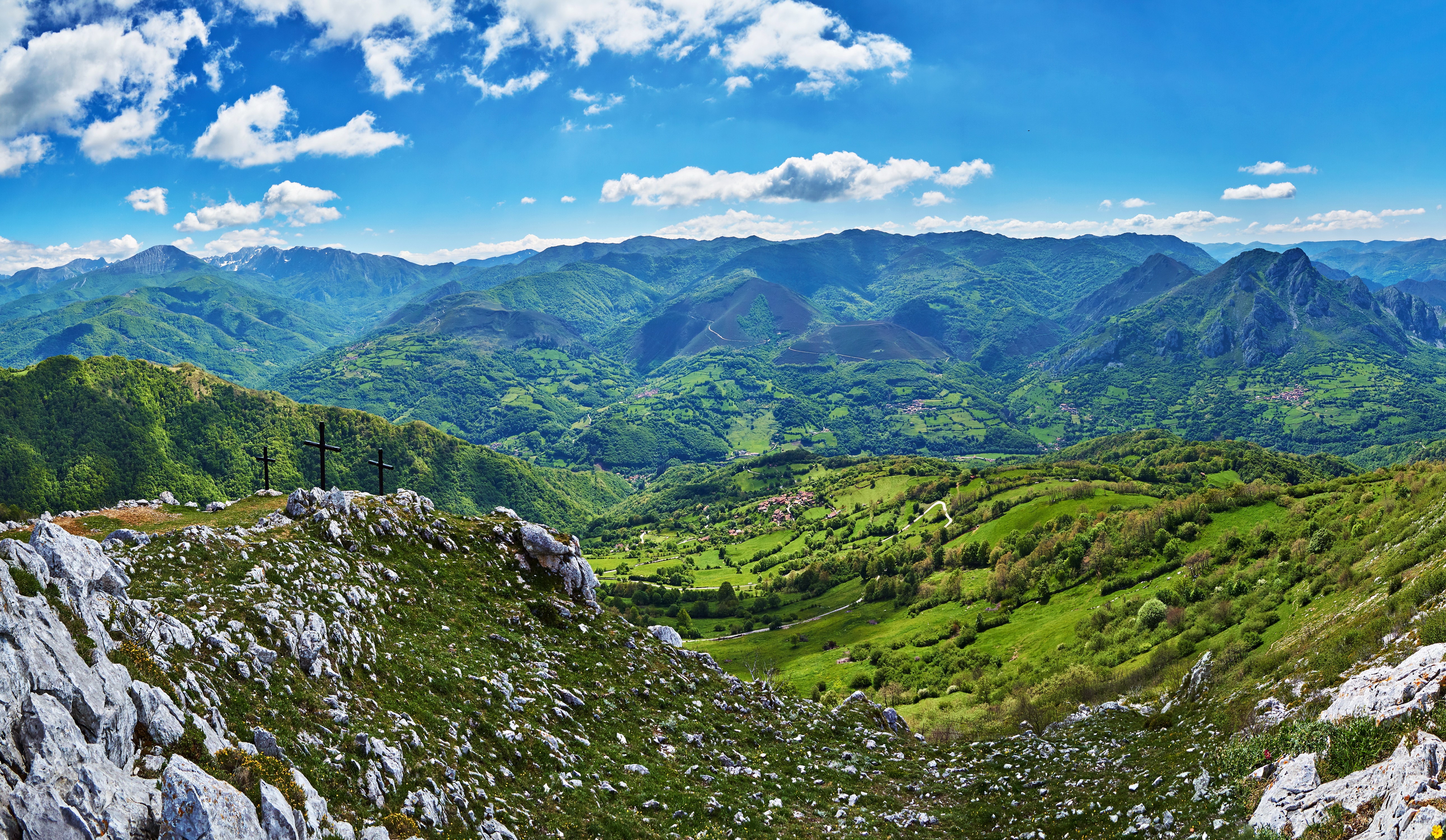 Three crosses on a mountain peak overlooking a green valley in Quiros, Spain HD Wallpaper