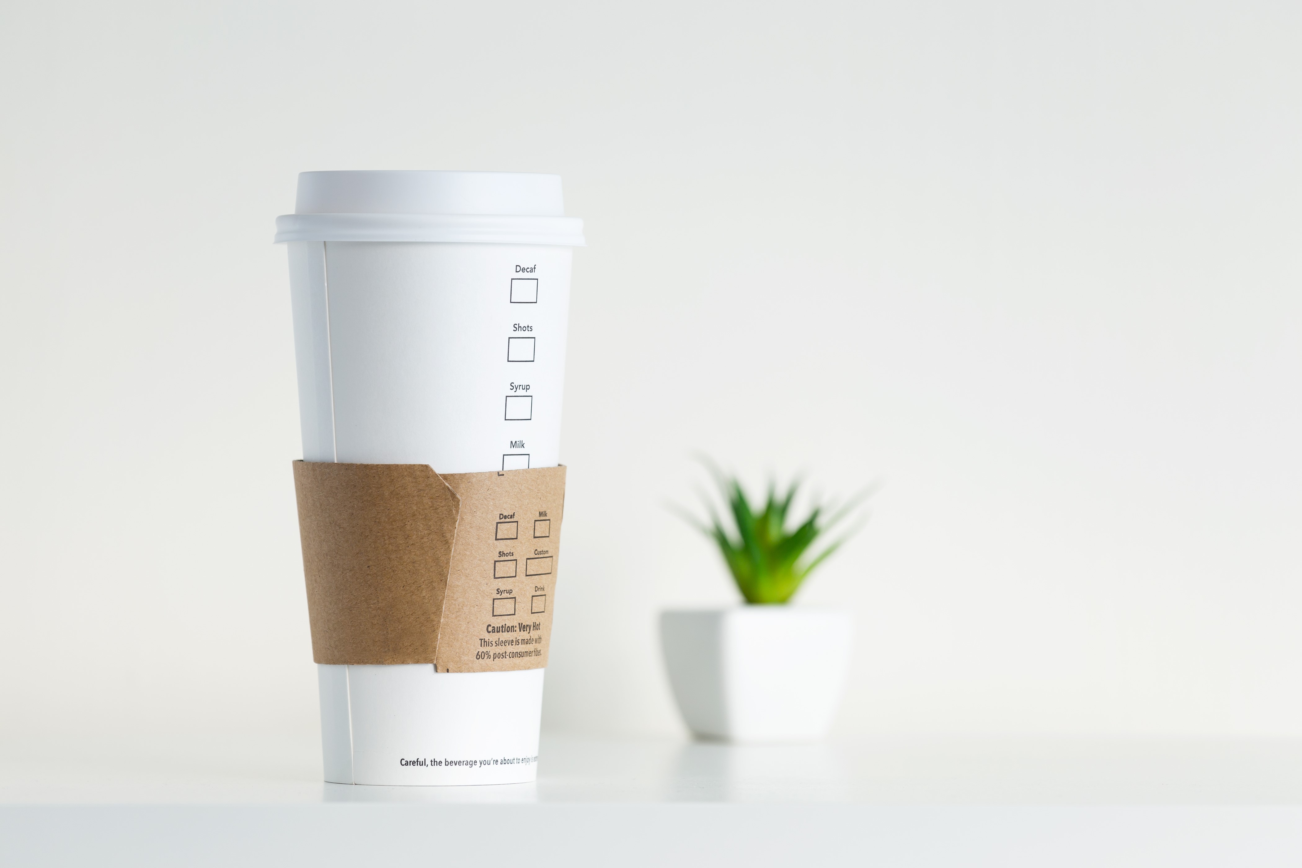 White coffee cup with sleeve and plant HD Wallpaper