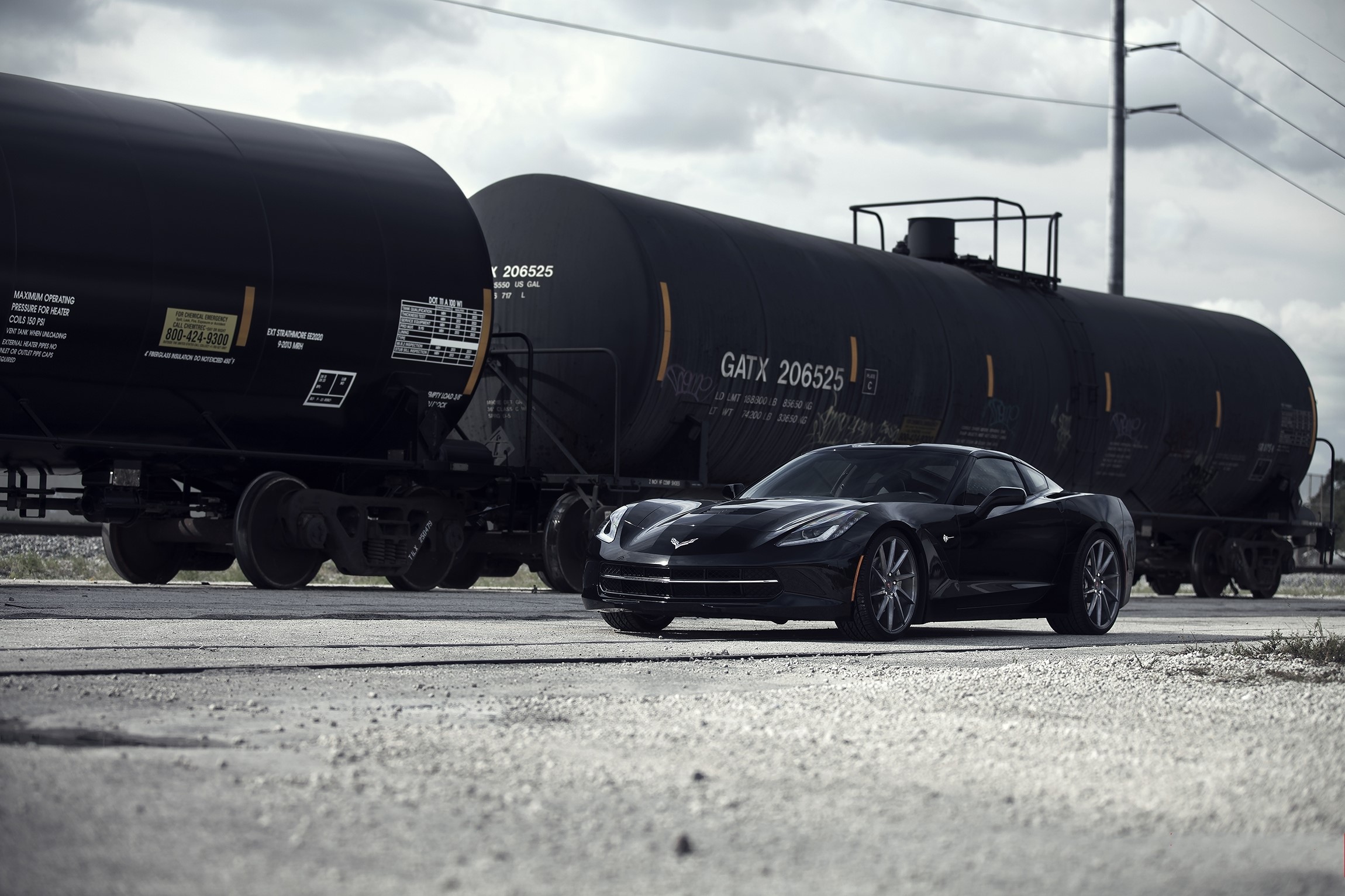 Black C7 Corvette Stingray next to train cars HD Wallpaper