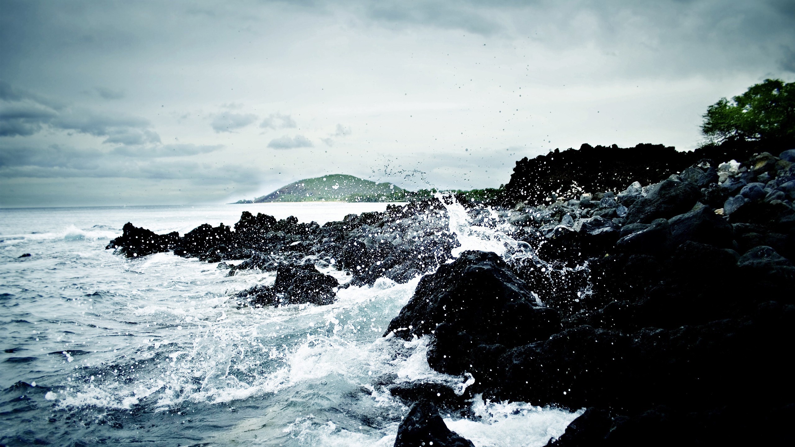 Waves crashing on dark volcanic rocks under a cloudy sky HD Wallpaper