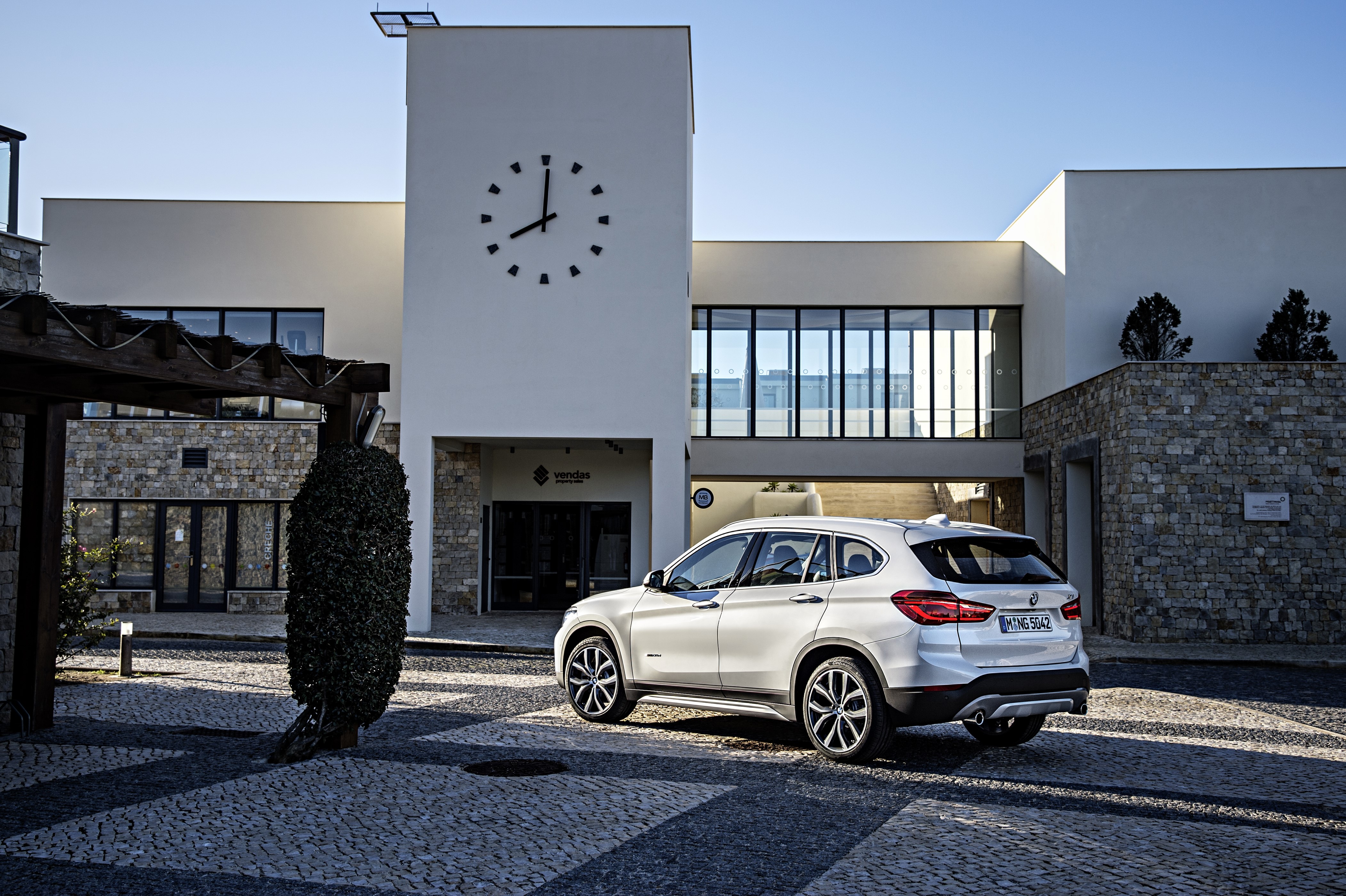 White BMW X1 xDrive20d parked in front of a modern building HD Wallpaper
