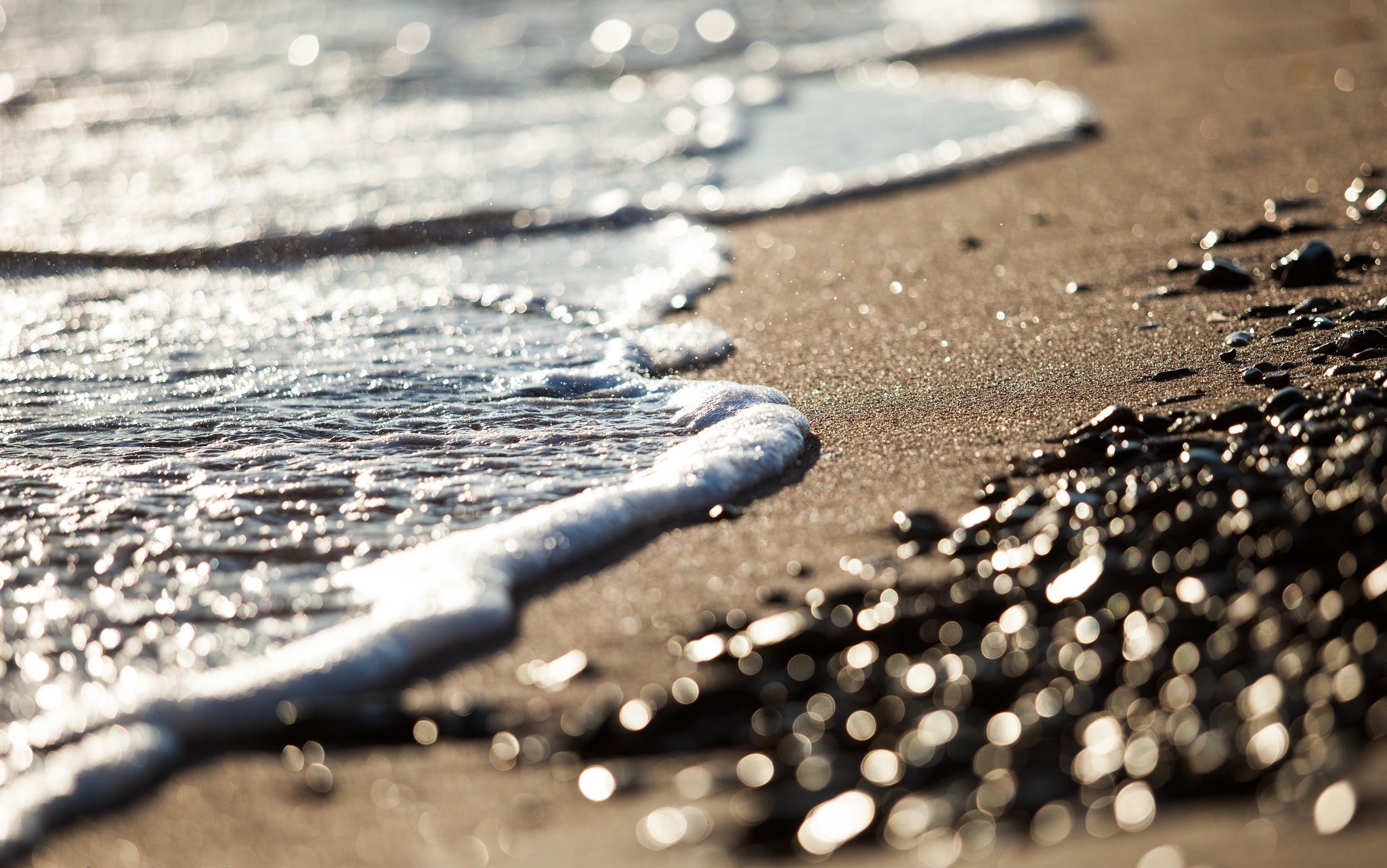 Close-up of waves washing onto a sandy beach with pebbles HD Wallpaper