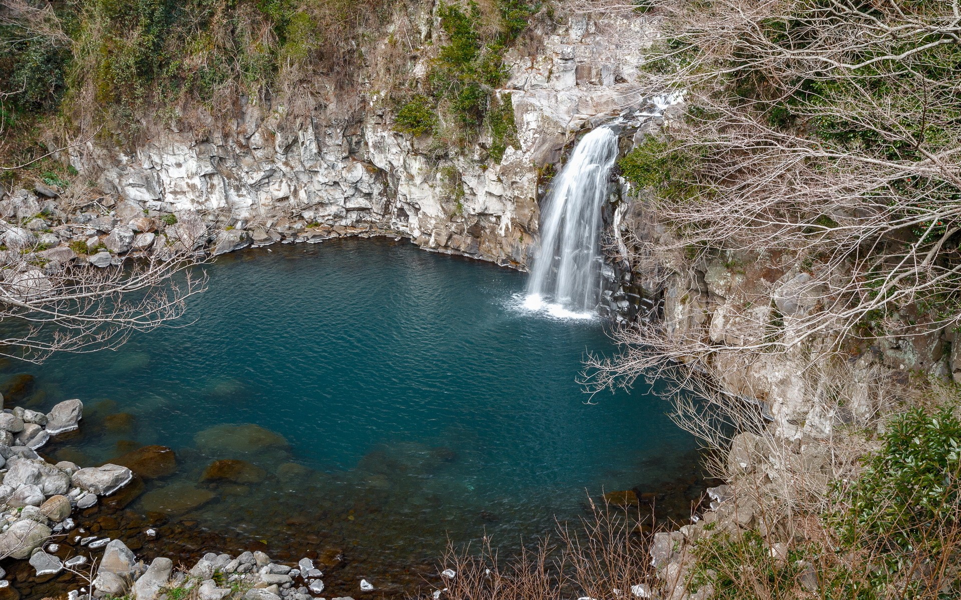 Waterfall cascading into a blue pool surrounded by rocks and trees HD Wallpaper