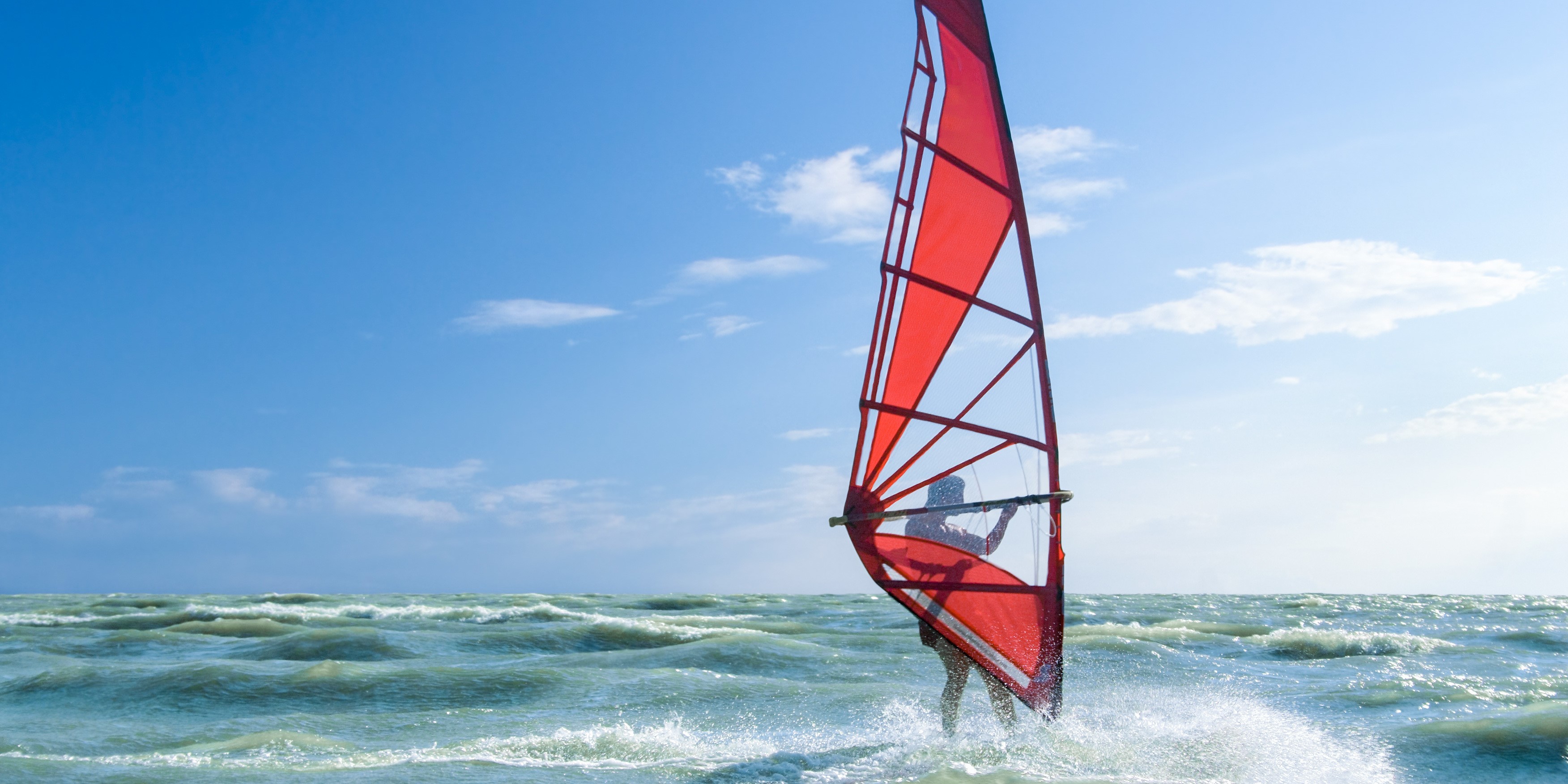 Windsurfer with red sail on wavy sea under blue sky HD Wallpaper