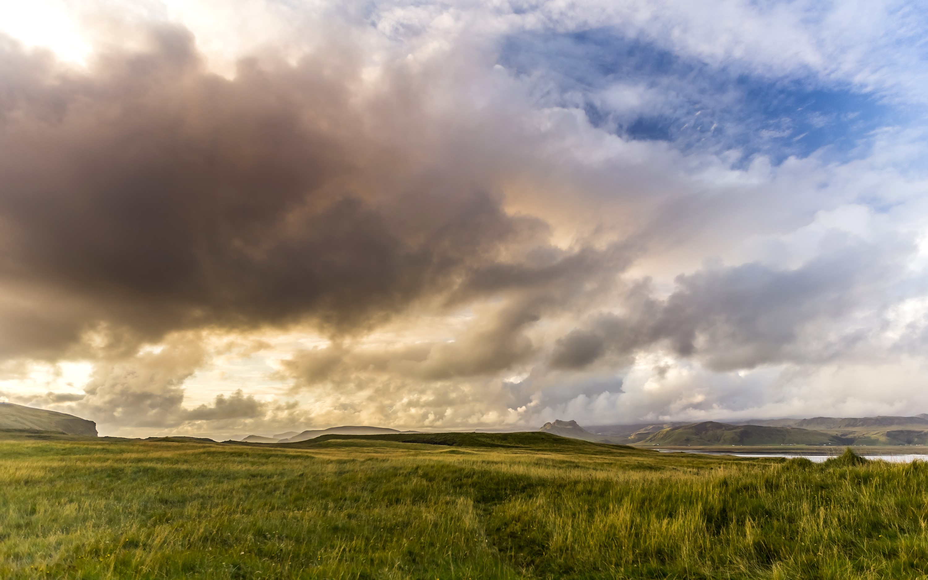 Grassy fields under dramatic clouds in Iceland HD Wallpaper