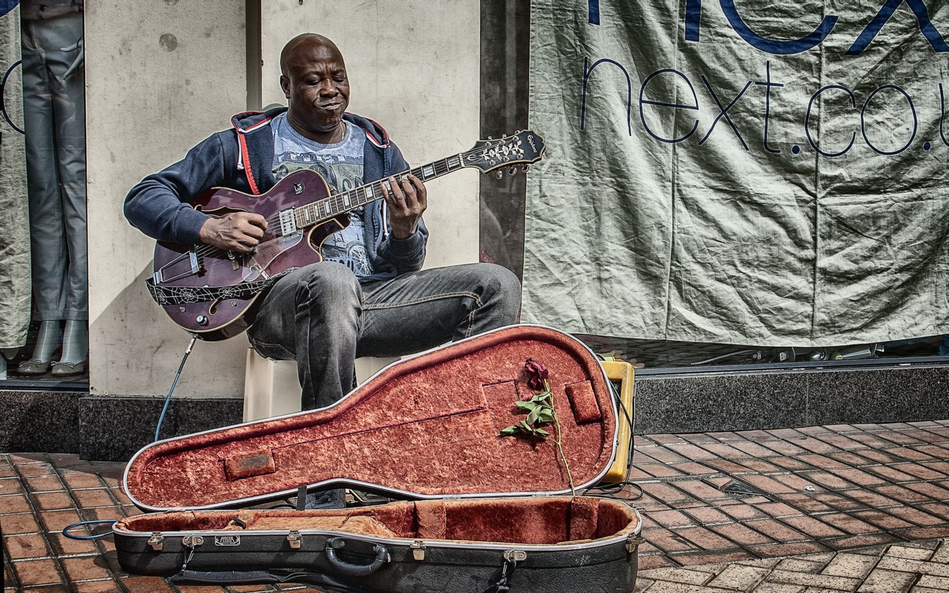Man playing guitar on street with guitar case HD Wallpaper