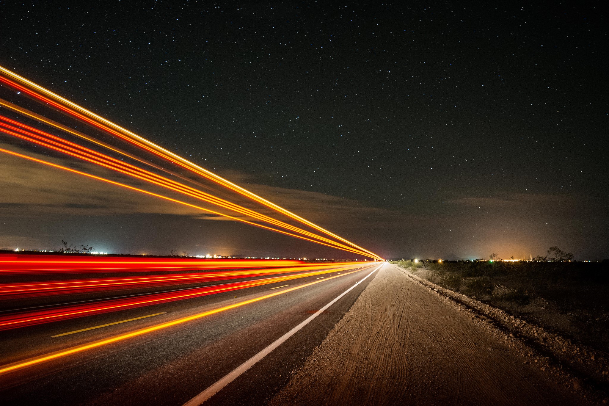 Light trails on a highway at night under a starry sky HD Wallpaper