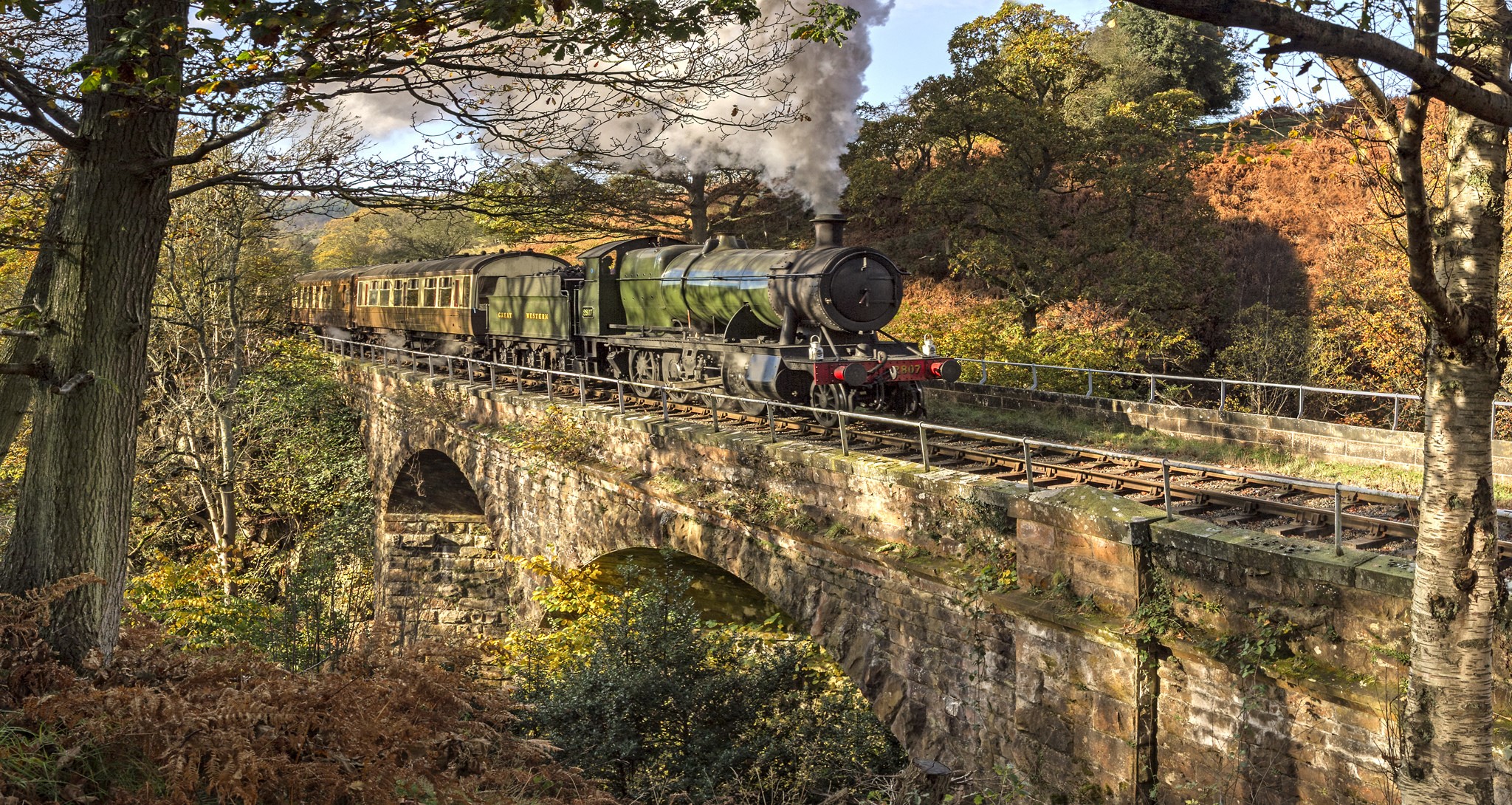 Steam train crossing a stone bridge in autumn HD Wallpaper