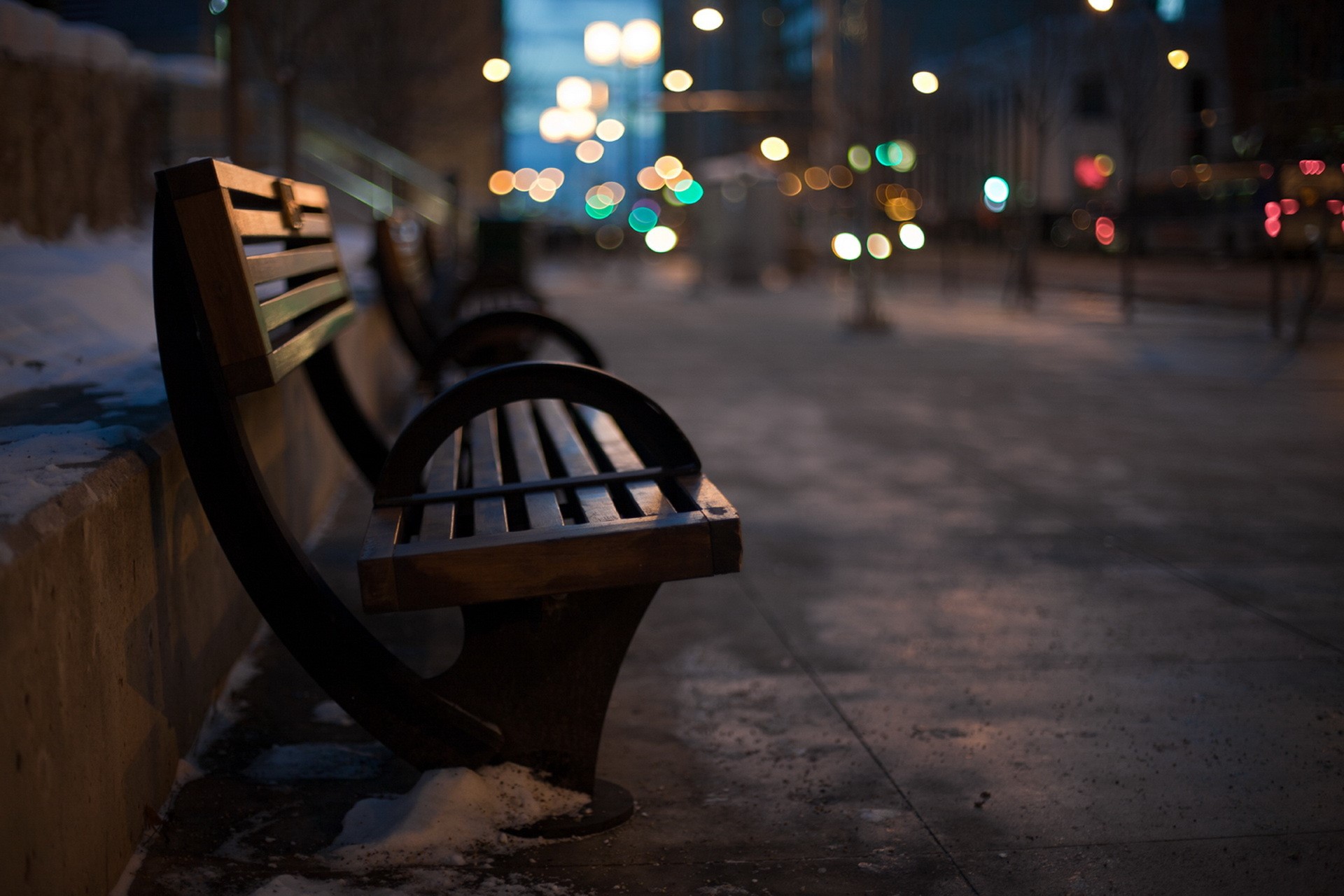 Empty park bench at night with city lights HD Wallpaper