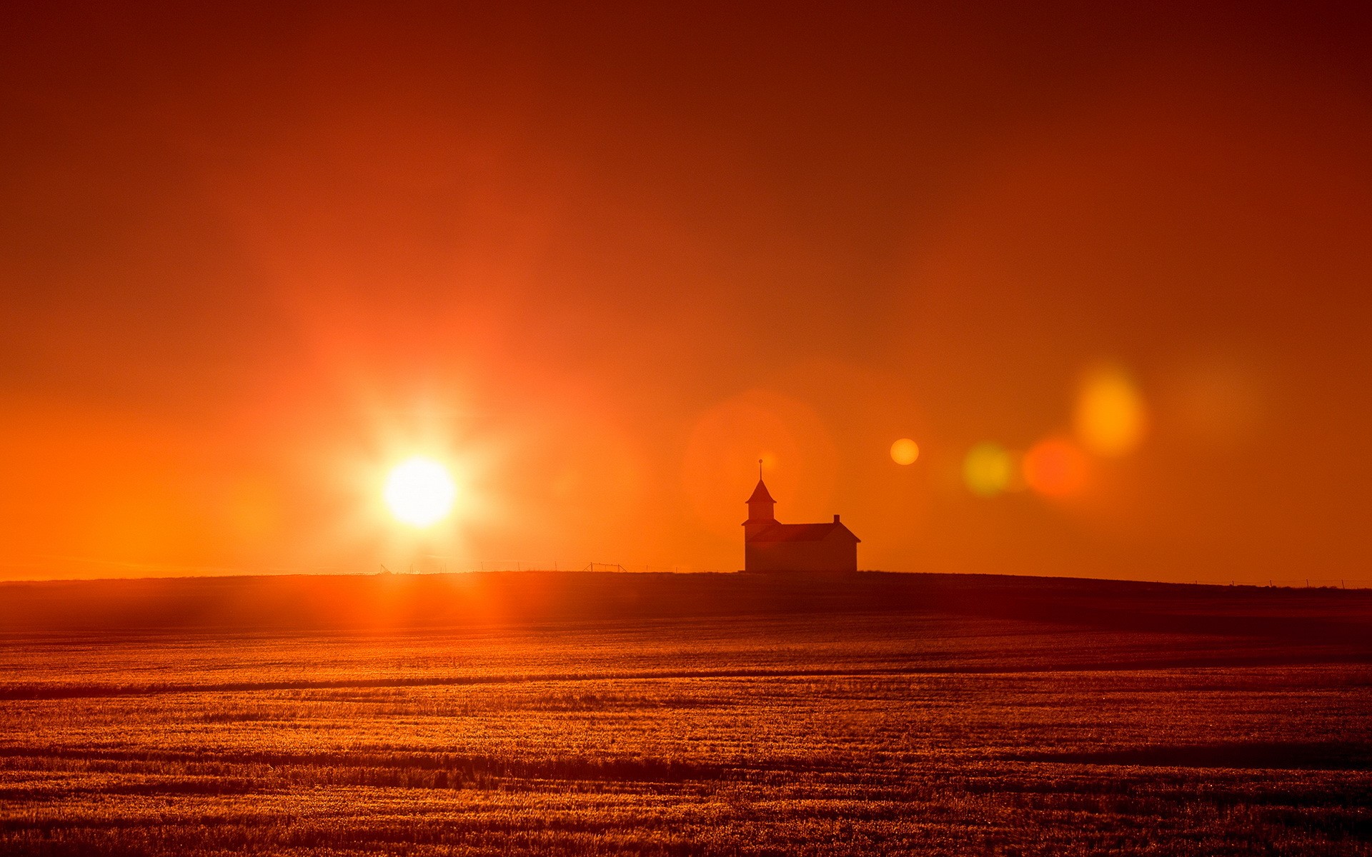Silhouette of a church against a vibrant sunset over a field HD Wallpaper
