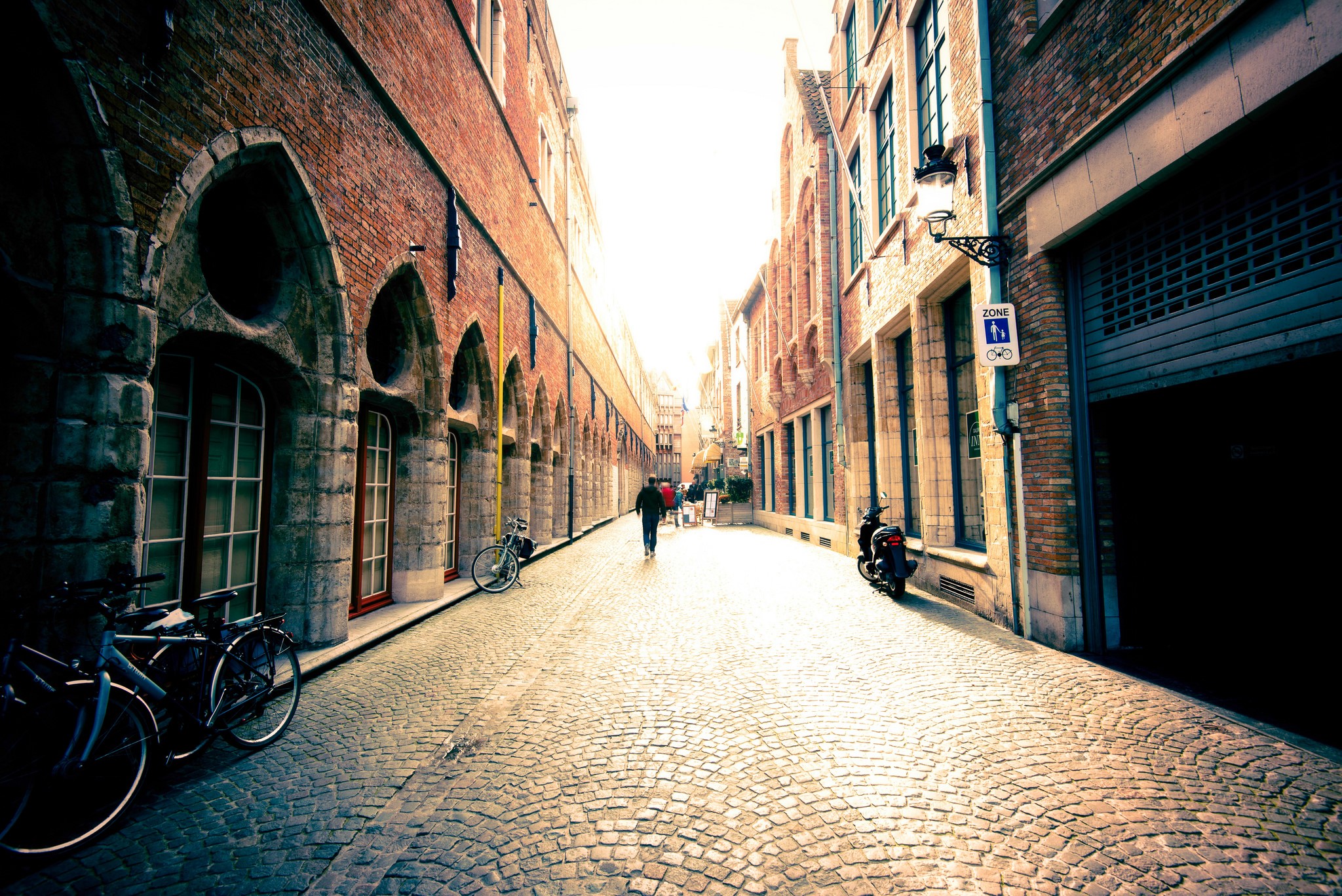 Cobblestone street in Bruges, Belgium with bicycles and scooters HD Wallpaper