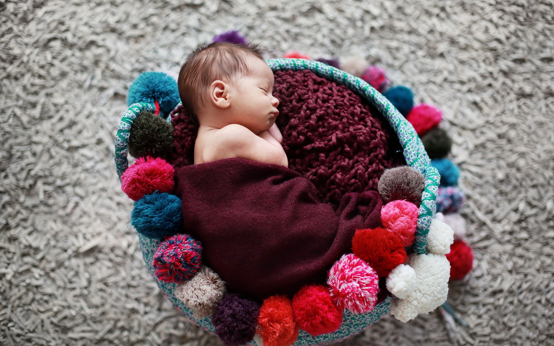 Newborn baby sleeping in a colorful pom-pom basket HD Wallpaper