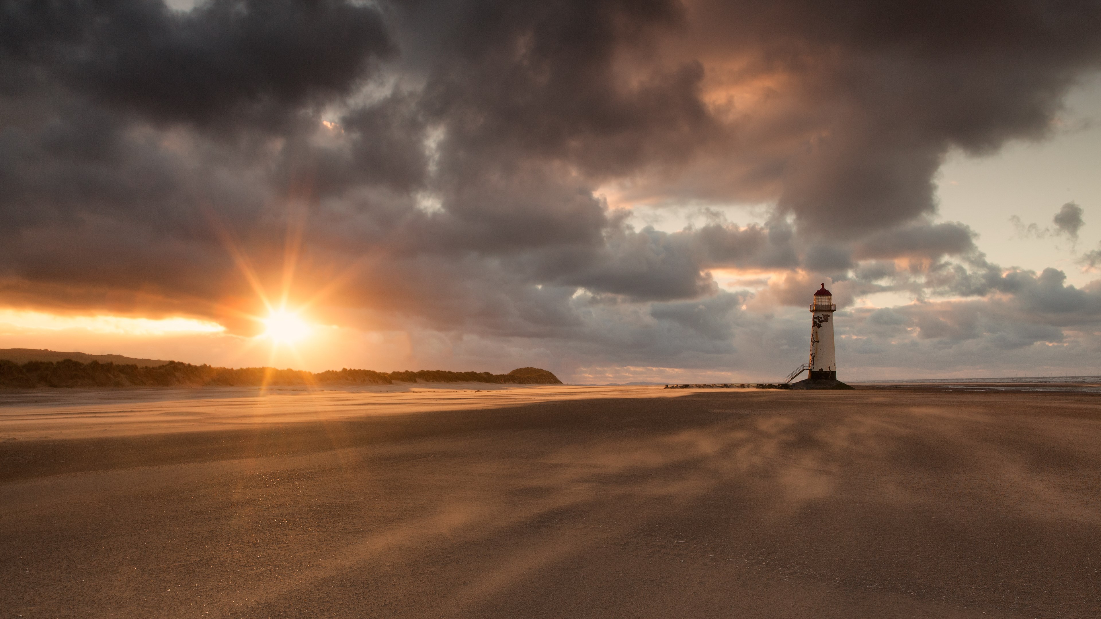 Lighthouse on a beach at sunset with dramatic clouds HD Wallpaper