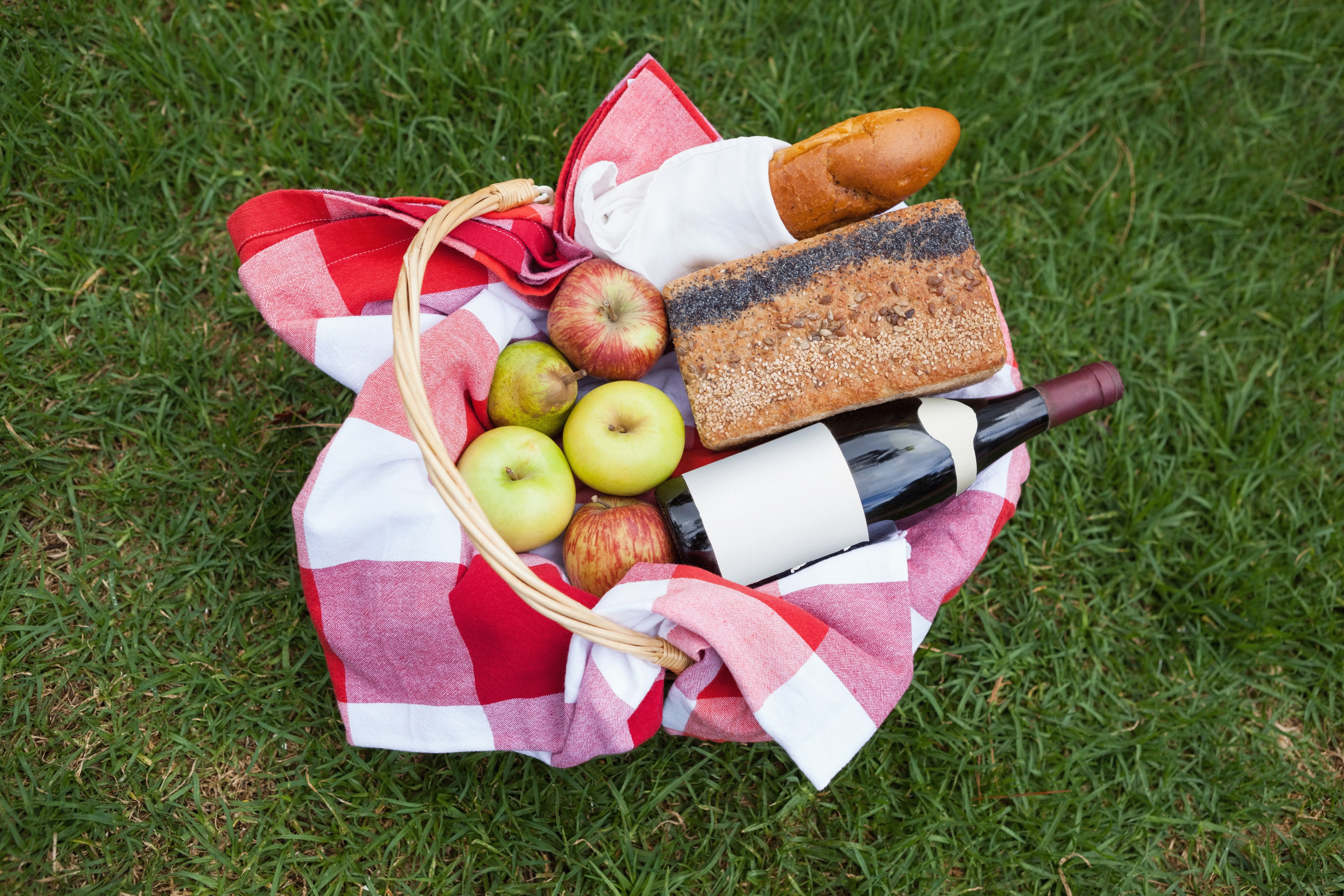 Picnic basket with wine, apples, and bread on grass HD Wallpaper