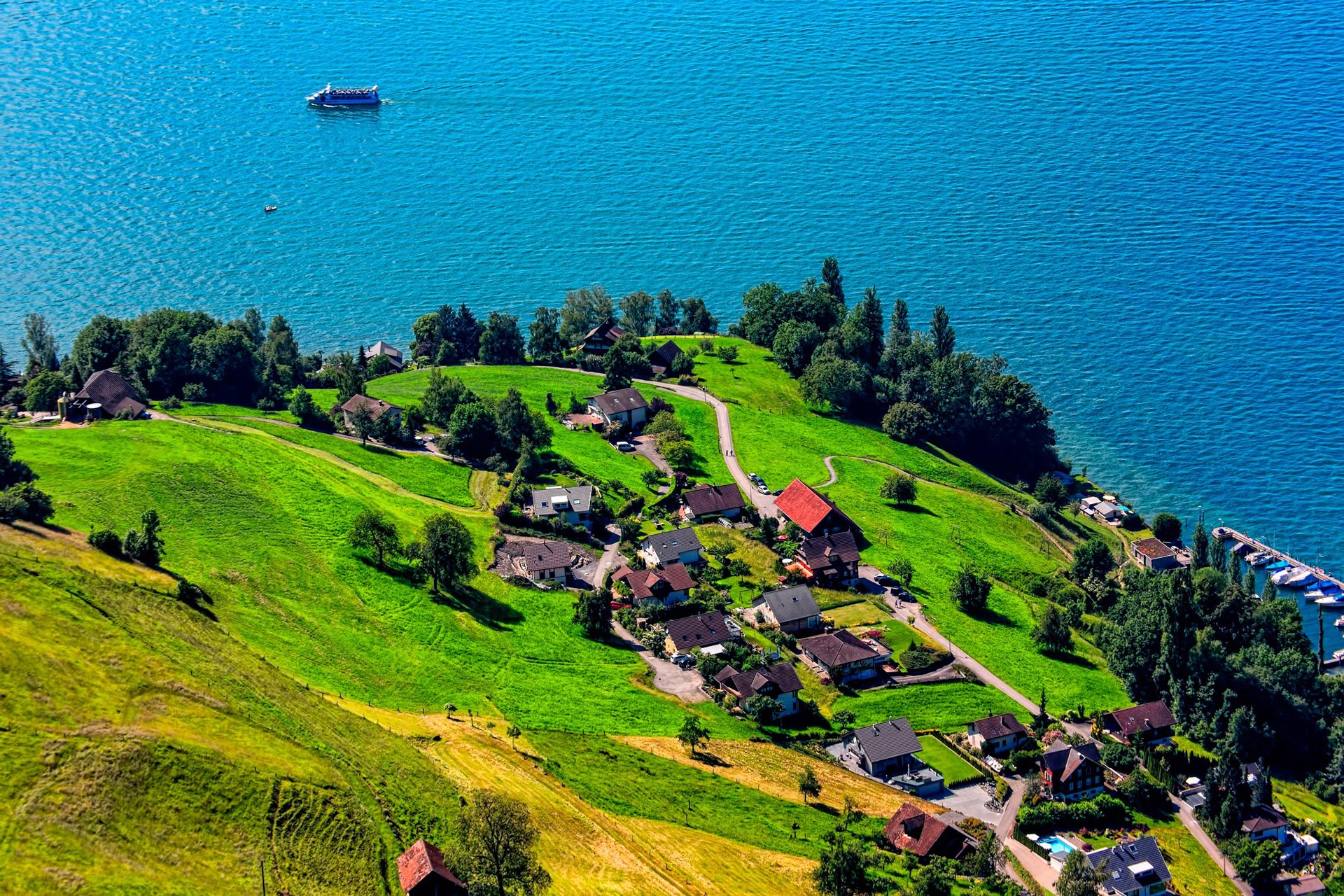 Houses on a green hill overlooking a blue lake HD Wallpaper