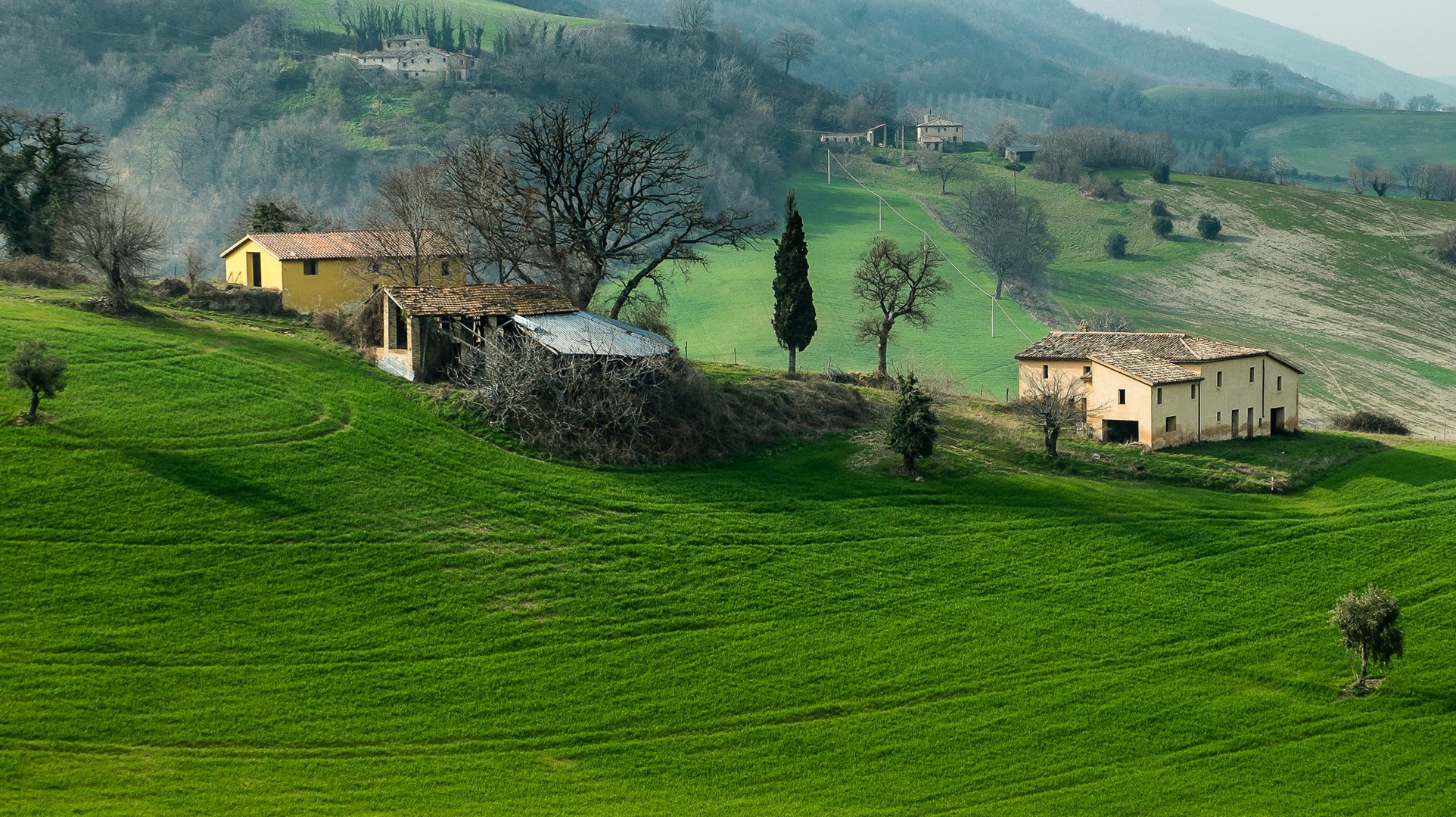 Italian countryside with rolling green fields and houses HD Wallpaper